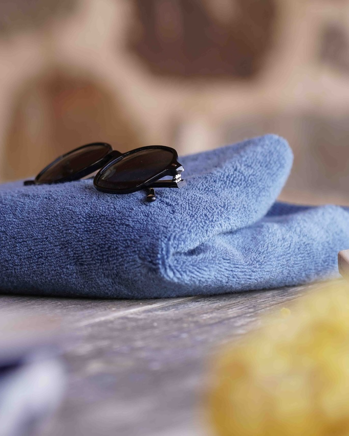 Blue towel with sunglasses on a surface, blurred stone wall in the background