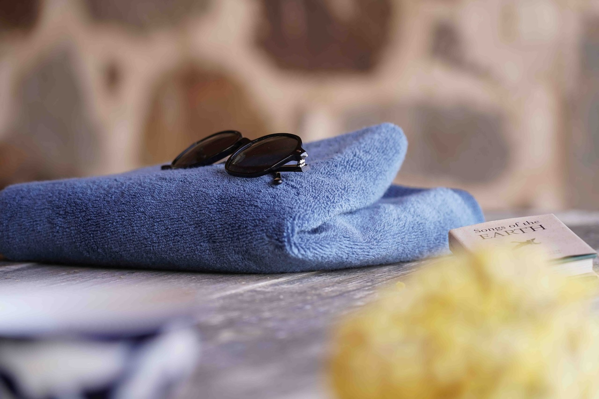 Blue towel with sunglasses on a surface, blurred stone wall in the background