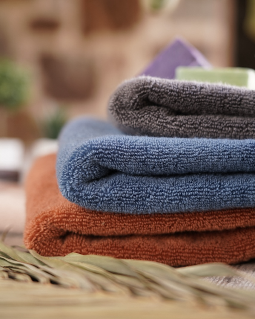 Stack of folded towels in orange, blue, and grey on a blurred natural background