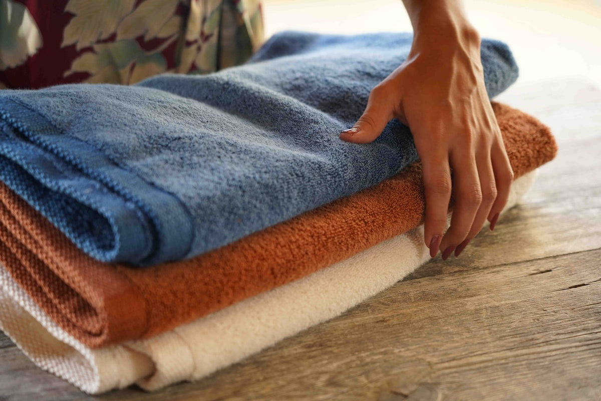 Stack of folded towels in blue, orange, and beige on a wooden surface with a hand reaching towards them.