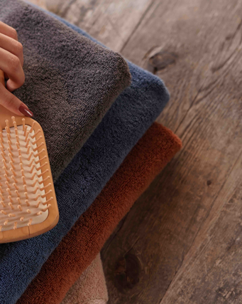 Hand holding a wooden brush over folded towels on a wooden surface