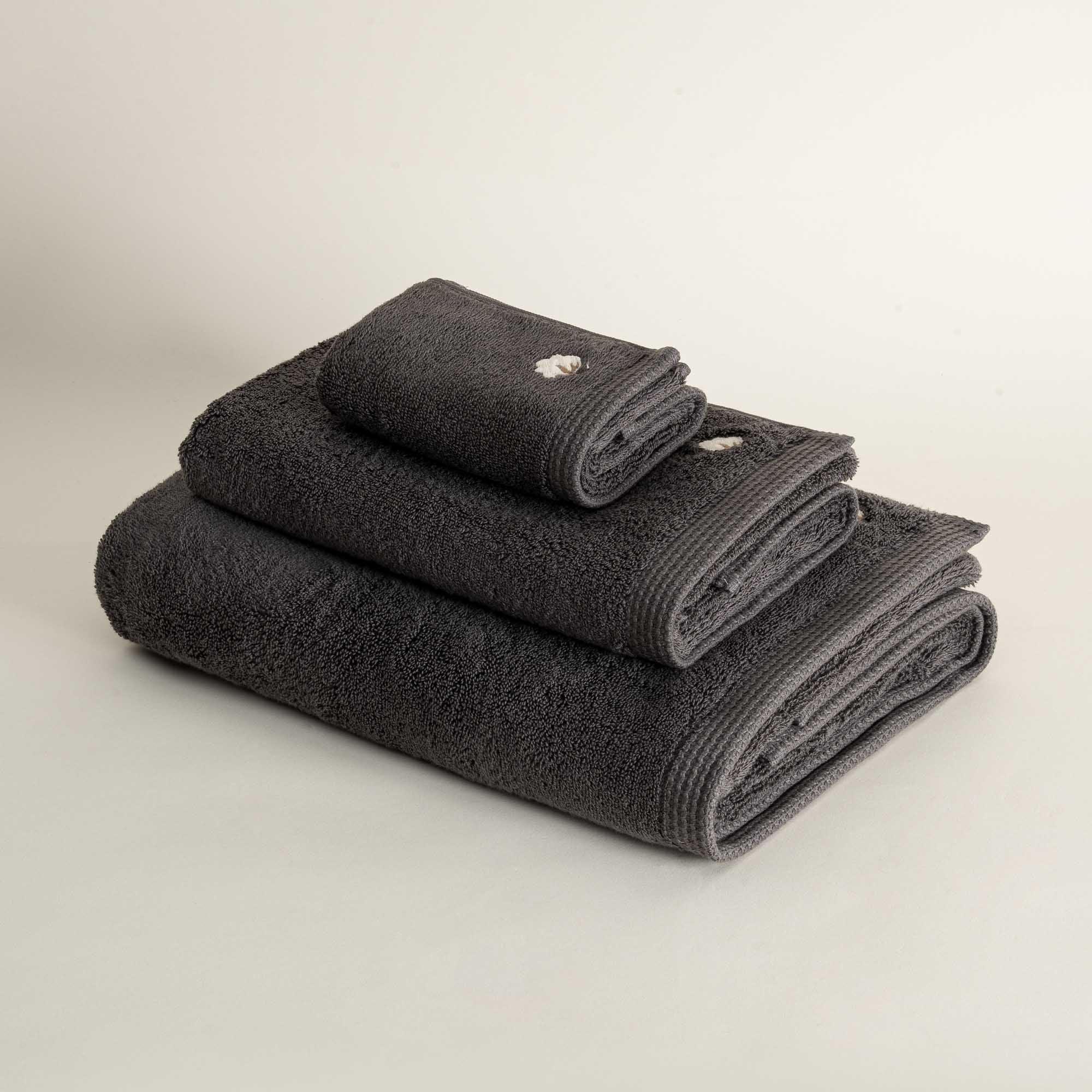 Side view of three folded Jasper 600-gram organic Aegean cotton luxury bath, hand, and washcloth towels in Charcoal Charm, highlighting soft plush texture, deep color, and luxurious fabric