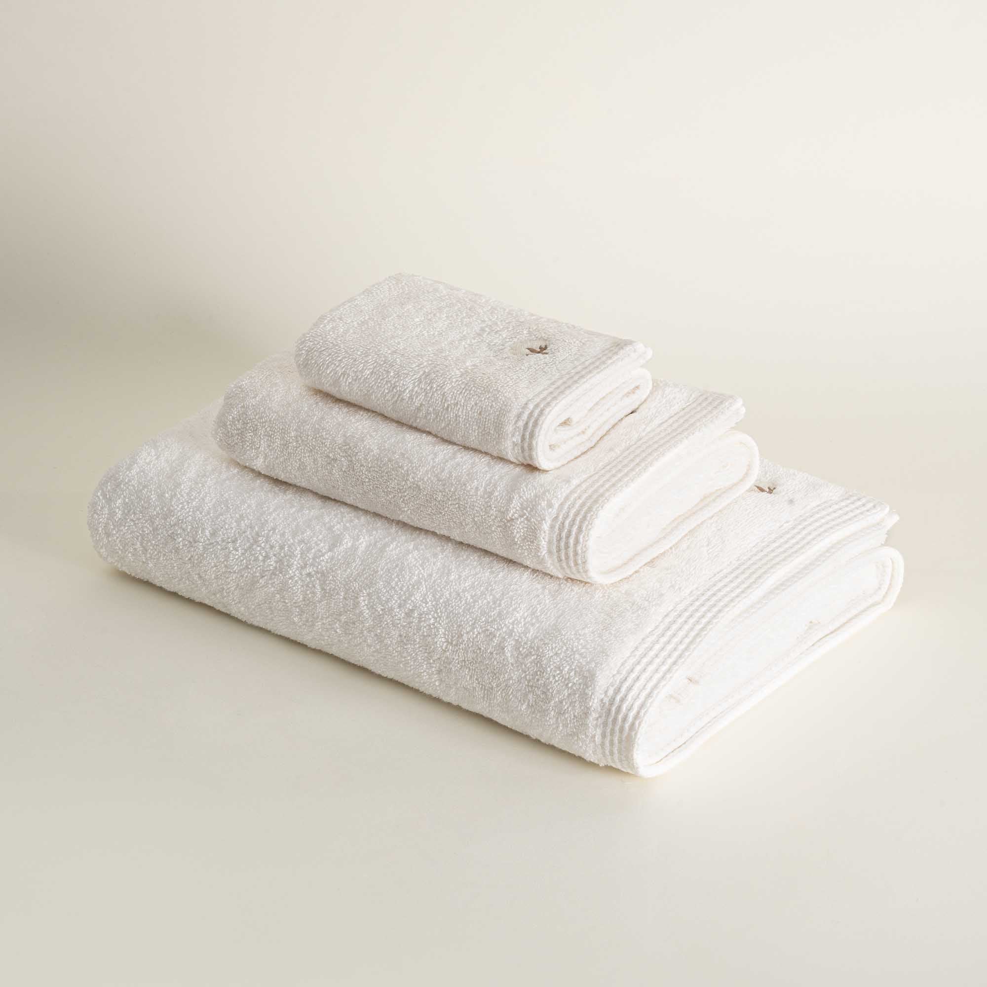 Side view of three folded Jasper 600-gram organic Aegean cotton luxury bath, hand, and washcloth towels in Ivory Embrace, highlighting soft plush texture, light tone, and luxurious fabric