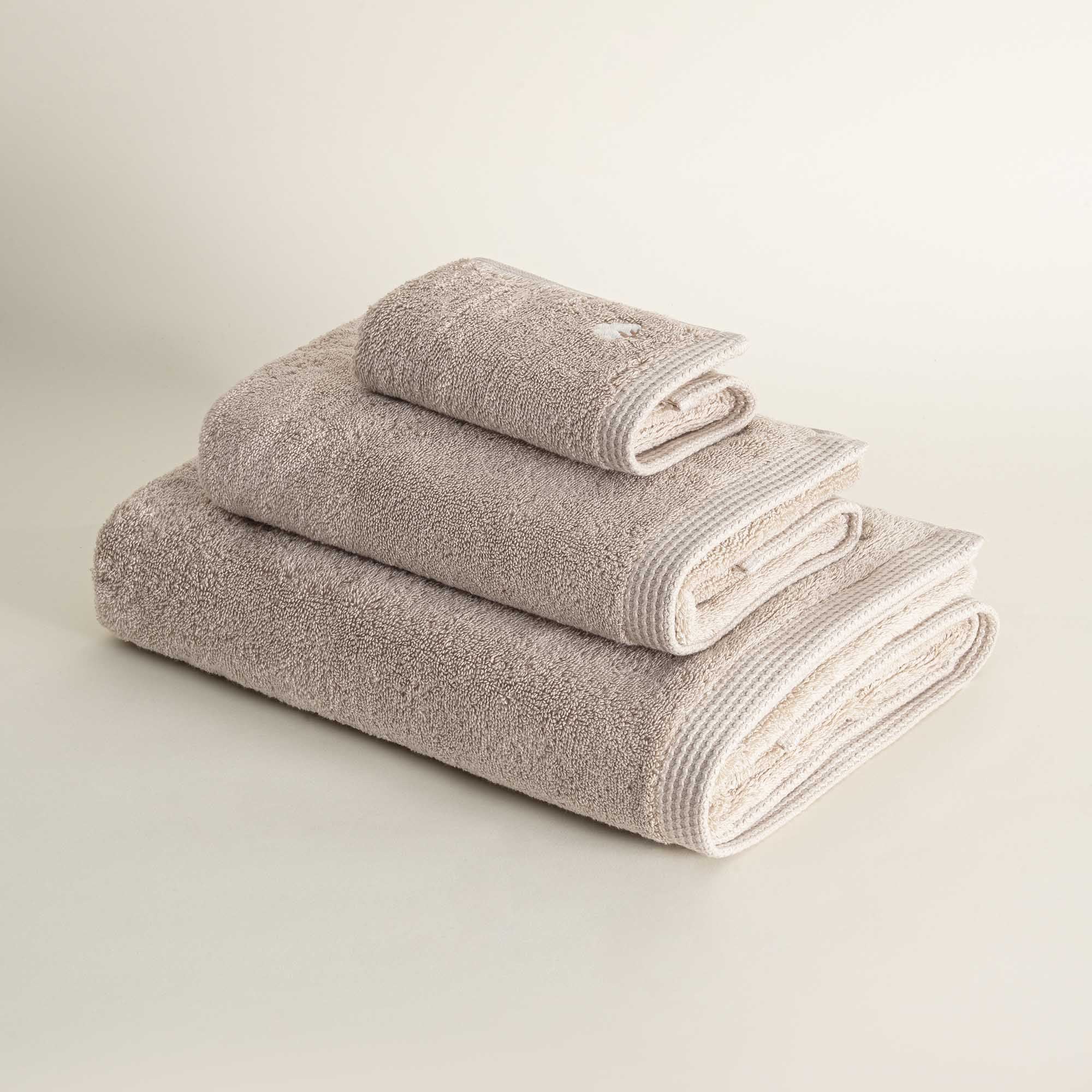 Set of three folded towels in beige on a light gray background