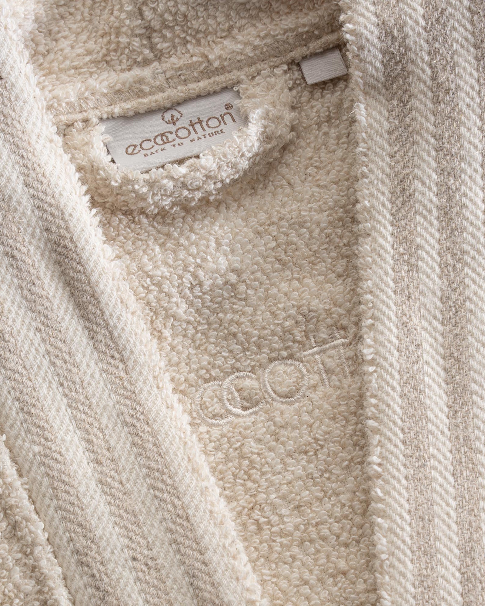 Close-up shot of Minoa's Raisa Hemp & Organic Cotton Mens Robe, a sustainable luxury bath robe, showcasing its EcoCotton brand tag and premium organic craftsmanship.