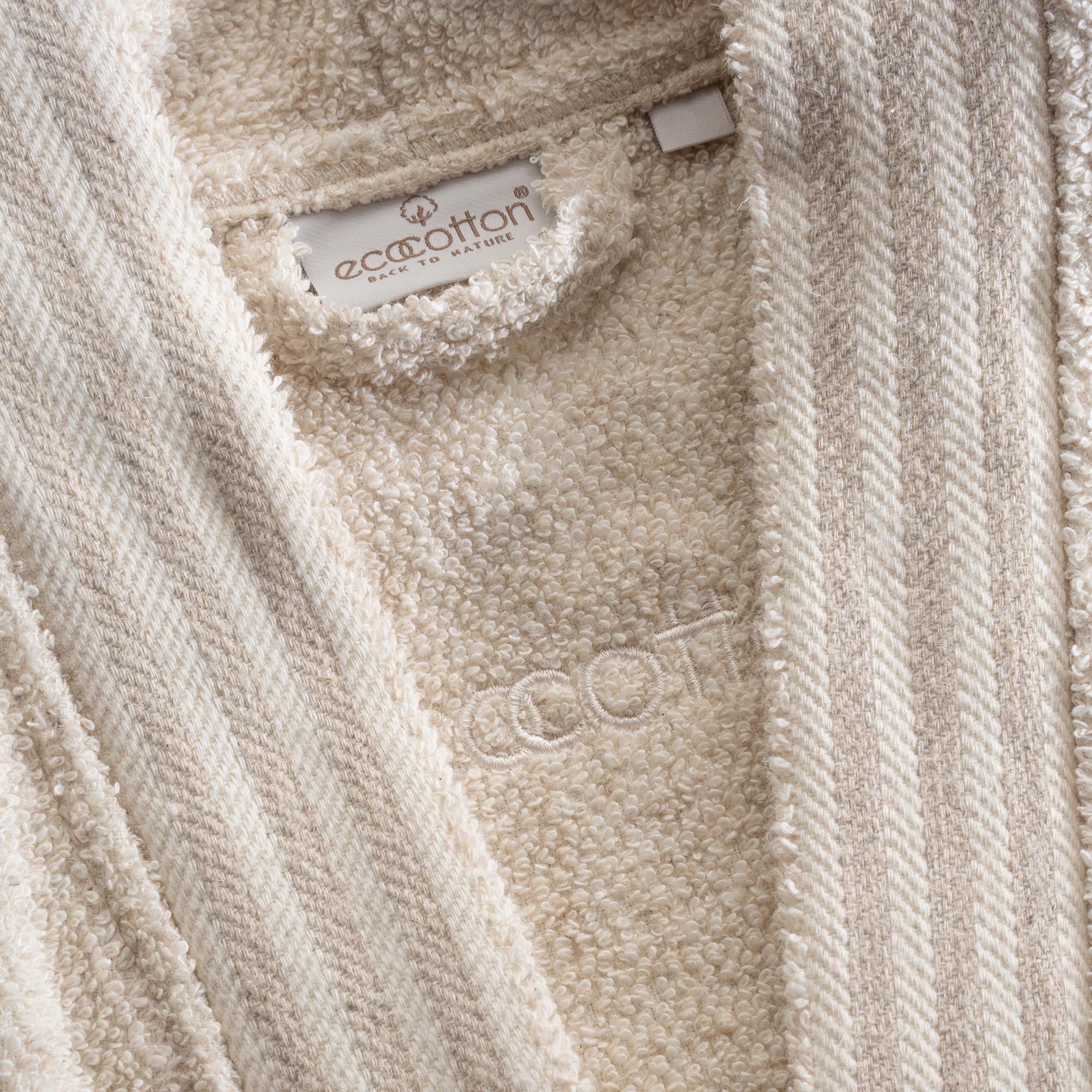 Close-up shot of Minoa's Raisa Hemp & Organic Cotton Mens Robe, a sustainable luxury bath robe, showcasing its EcoCotton brand tag and premium organic craftsmanship.