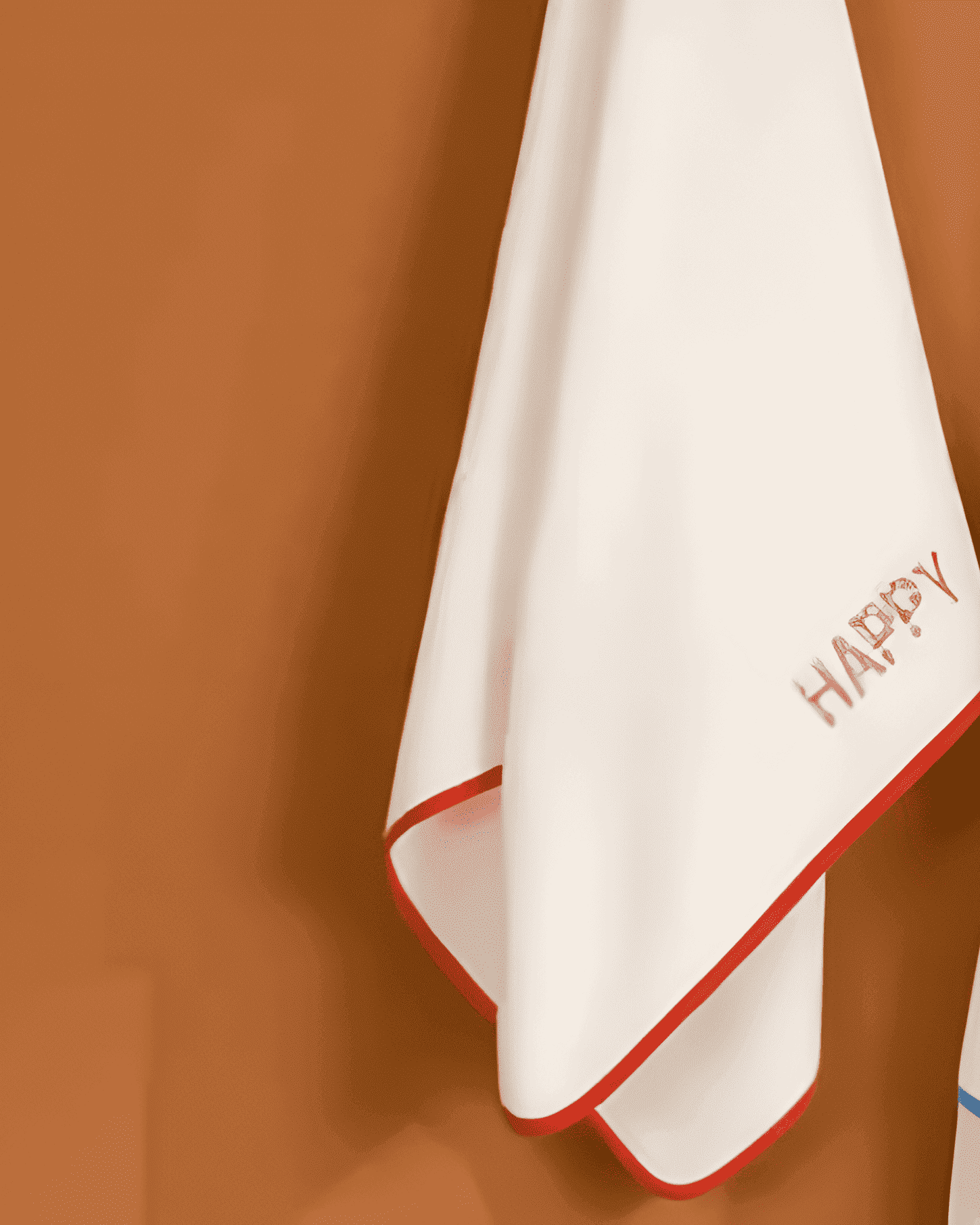 White towel with red border and 'HAPPY' text on a brown background