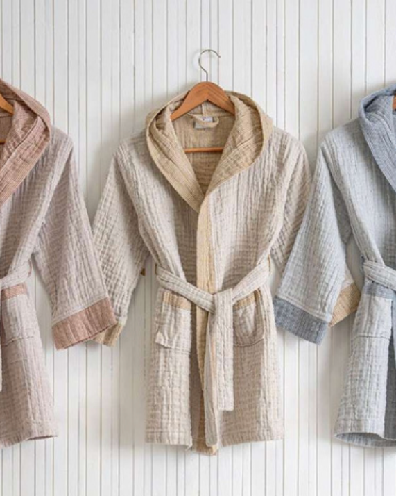 Three bathrobes hanging against a striped background, in beige, gray, and blue colors, all with a hood and sash belt.