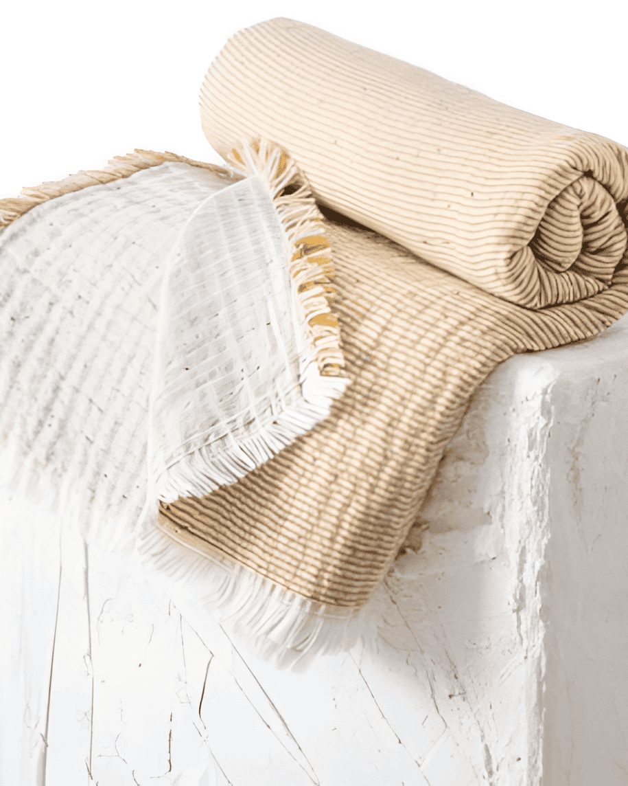 Two folded blankets, one white with fringes and the other beige, on a light wooden surface.