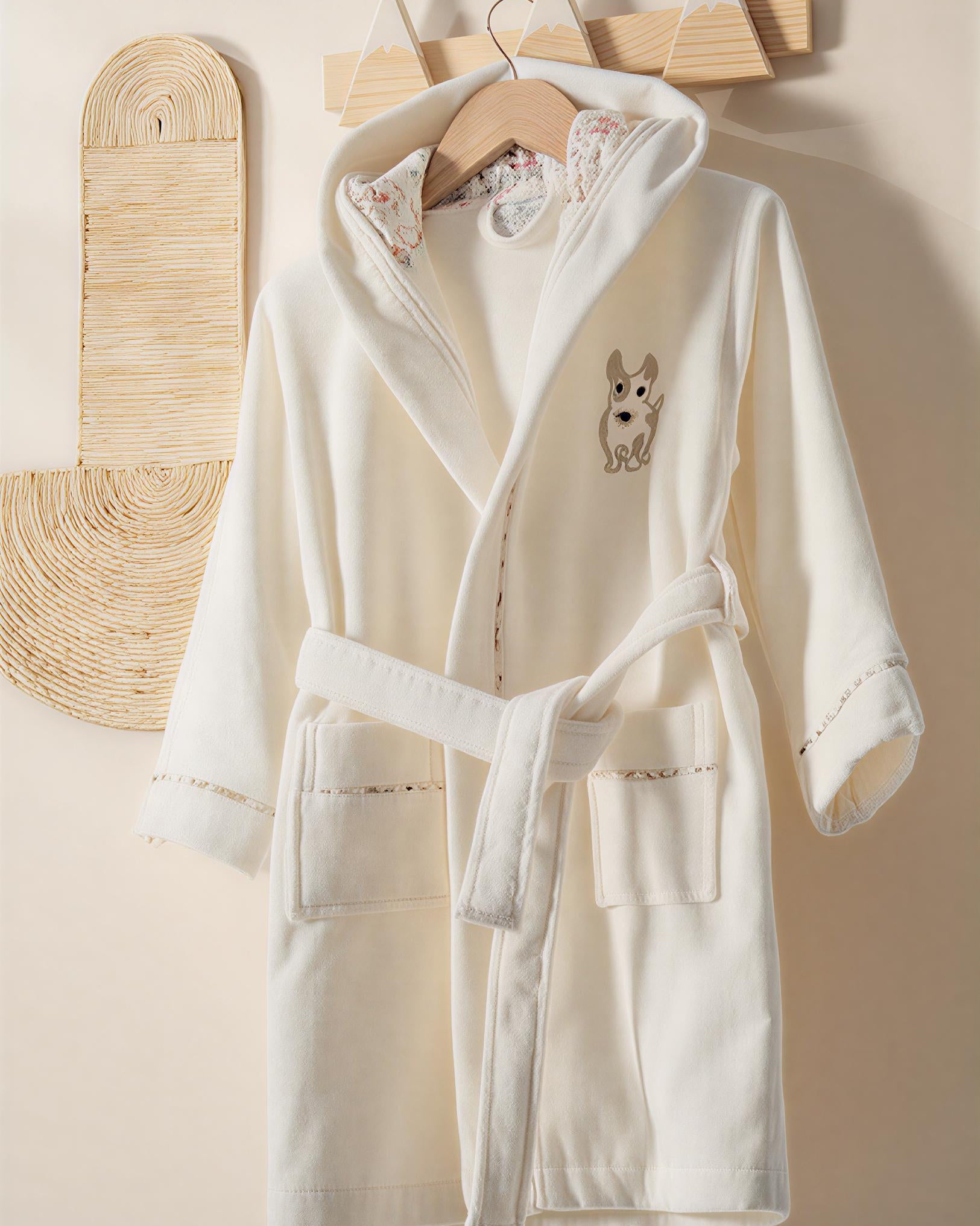 White robe with dog embroidery on a wooden hanger against a beige wall.