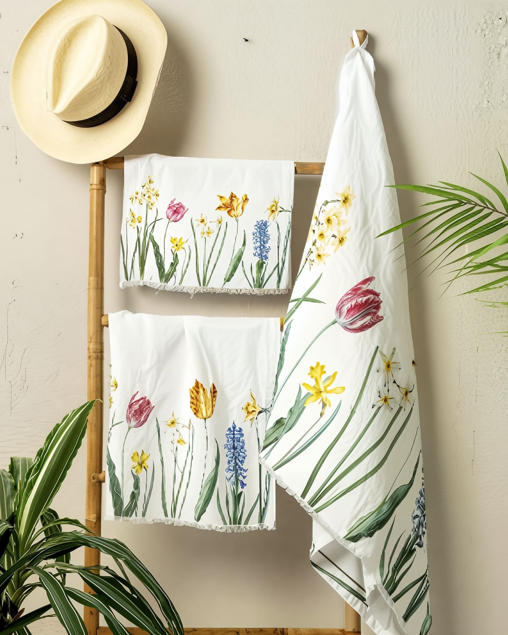 Floral-patterned towels hanging on a rack with a hat and plants in the background.