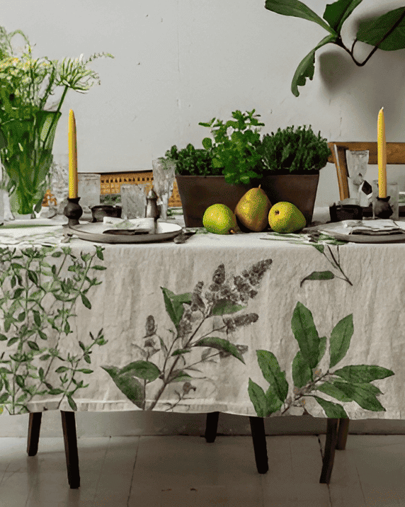 Dining table set with a botanical print tablecloth, candles, fruit, and wine glasses.