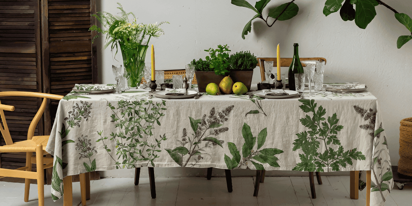 Dining table set with a botanical print tablecloth, candles, fruit, and wine glasses.