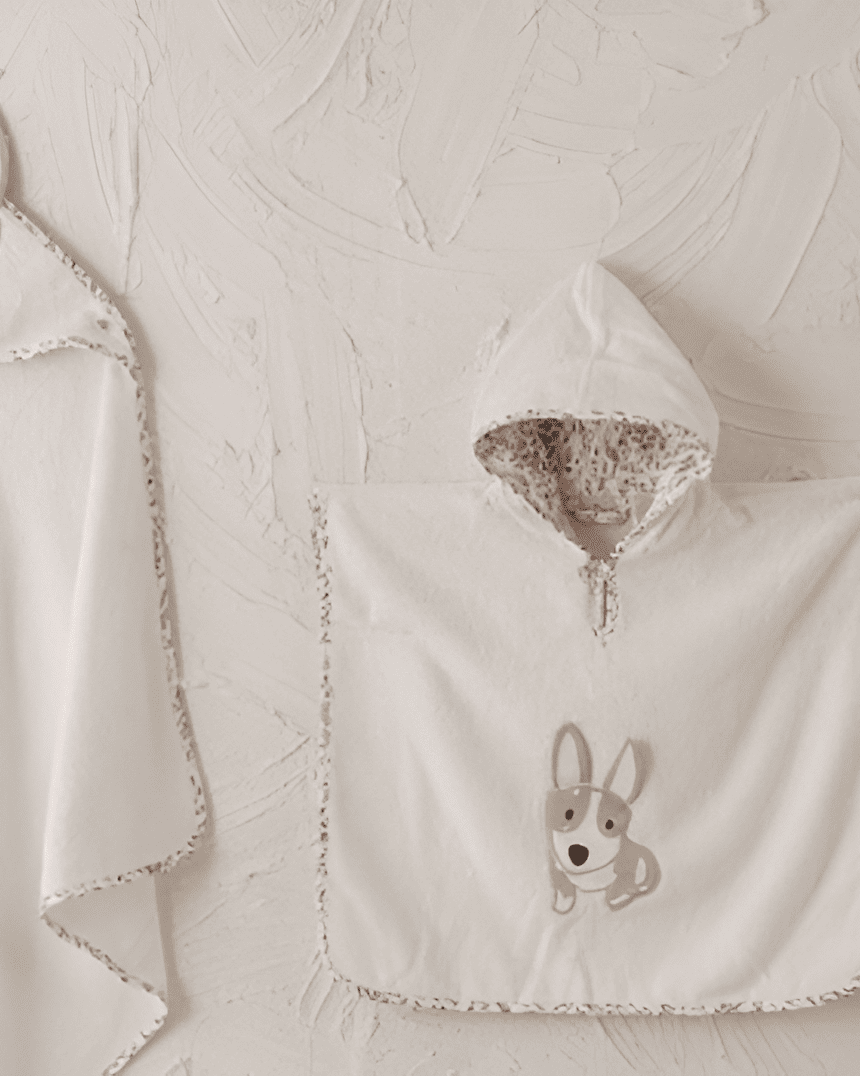 Baby blanket, hooded towel, and bib with dog design on a textured beige background