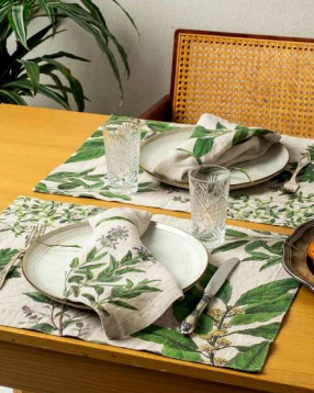 Dining table set with green leaf-patterned placemats, plates, and glasses.