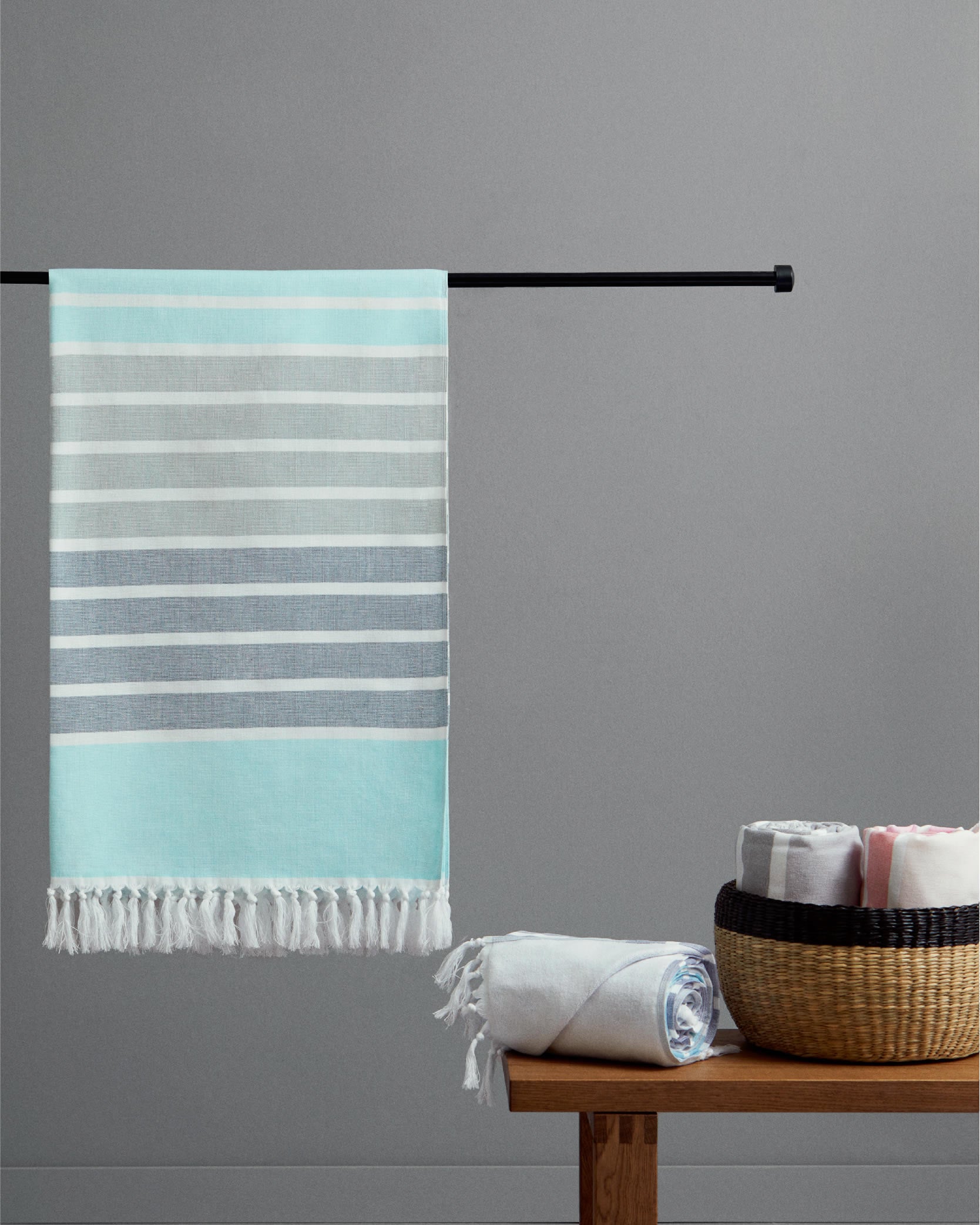Striped towel hanging on a rod with additional towels on a wooden table against a gray wall.