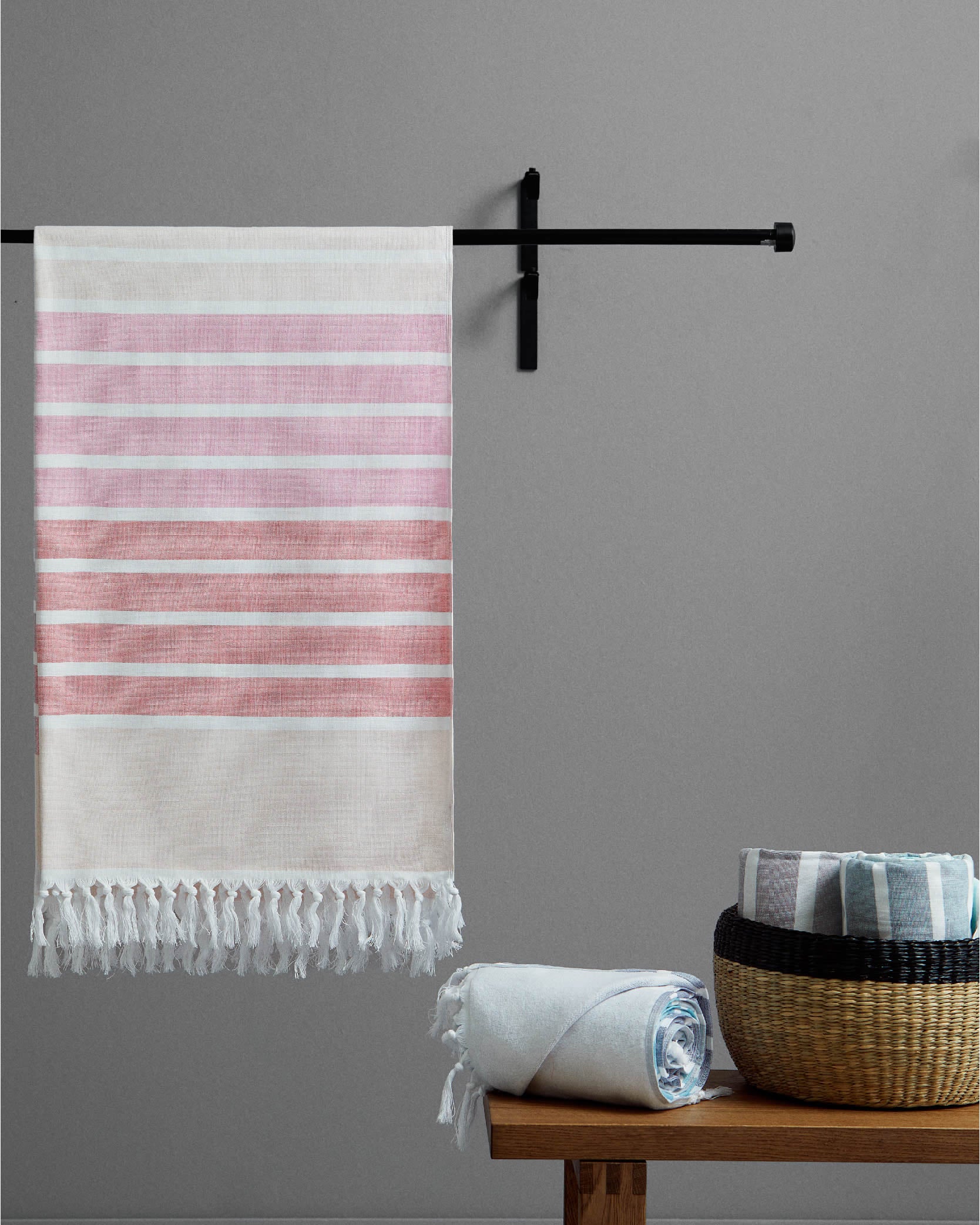 Striped towel hanging on a rack with a wooden table and basket in the foreground against a gray wall.