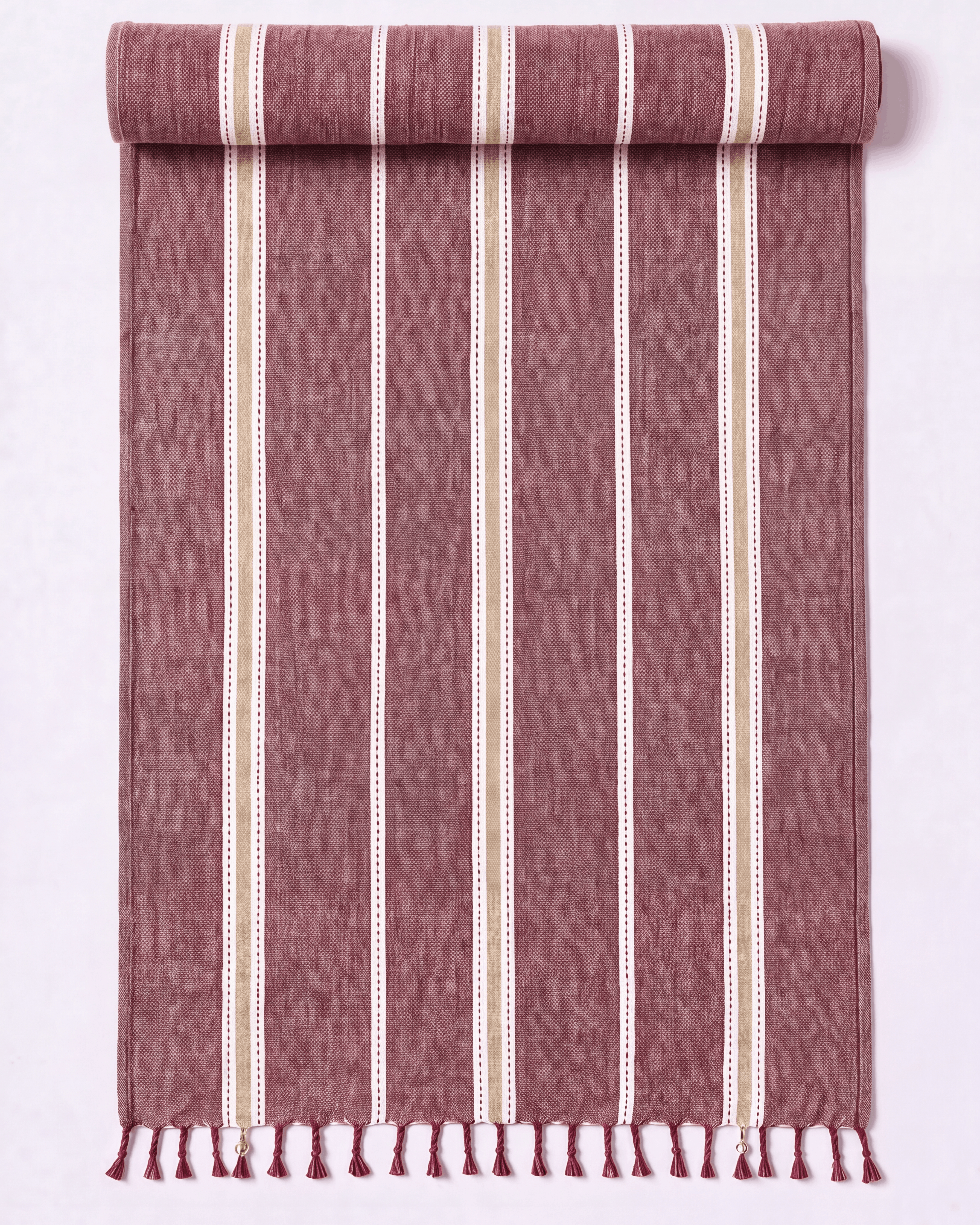A rolled and unrolled woven towel featuring vertical stripes in dusty rose, cream, and white. The fabric has a textured ikat-like weave and finished with a fringed tassel edge at the bottom, displayed against a clean white background.