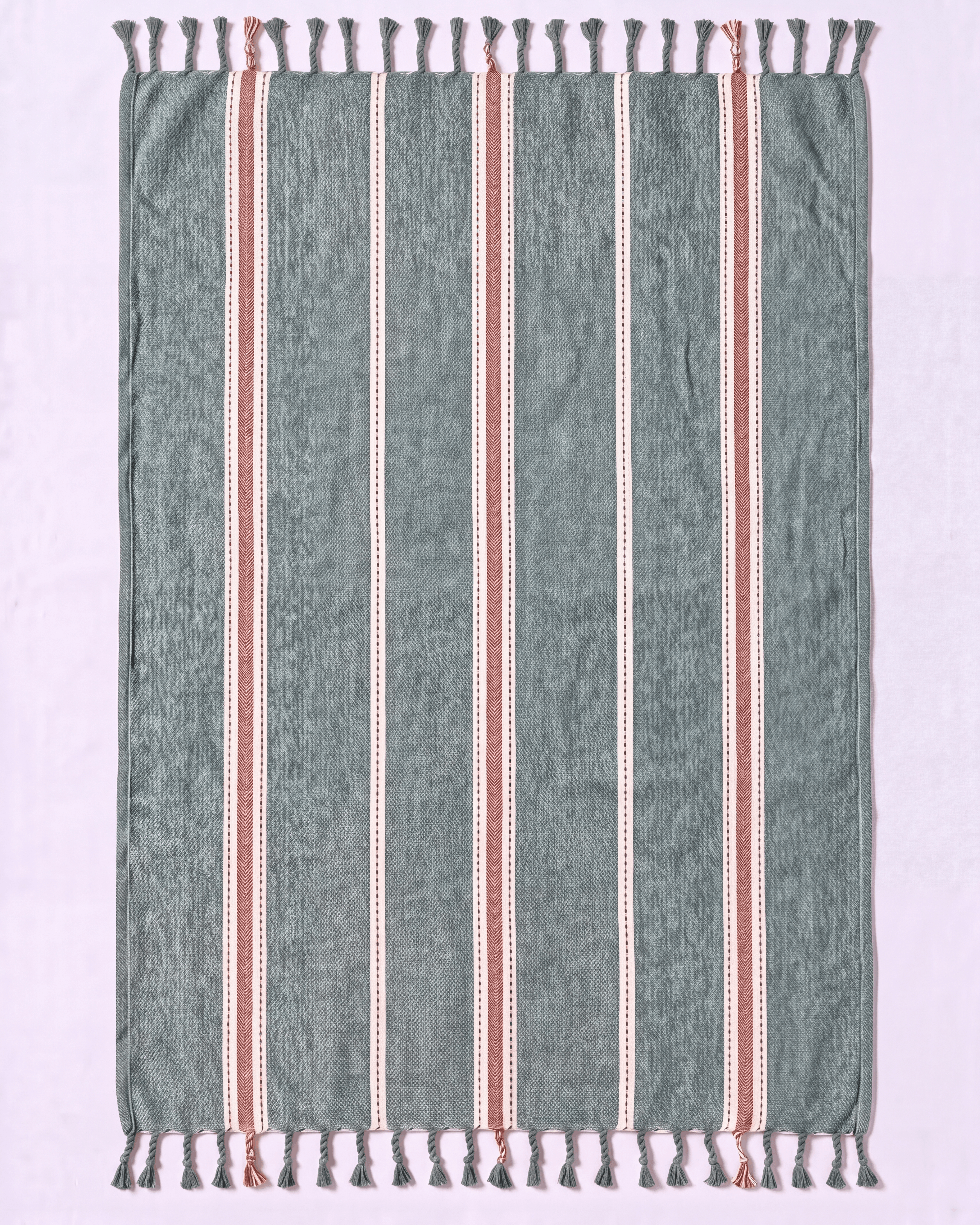 A rectangular woven towel with fringe tassels on both ends, featuring a muted sage green base with vertical stripes in white and terracotta red.