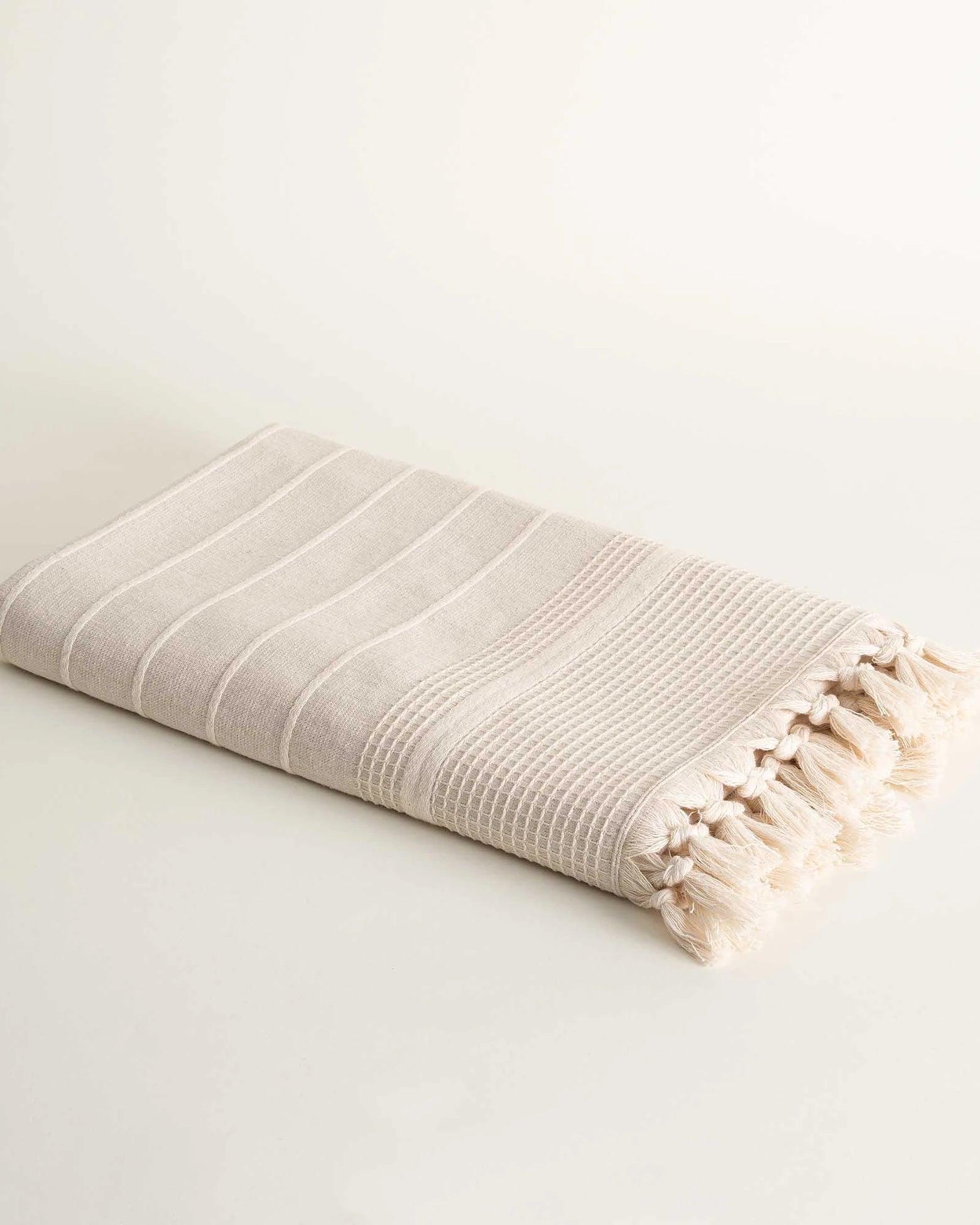 Folded Arden Hemp and Organic Cotton Bath Towel with tassels in sand and white highlighting the soft texture natural color and elegant tassel details of this luxury bath towel and organic bath towel