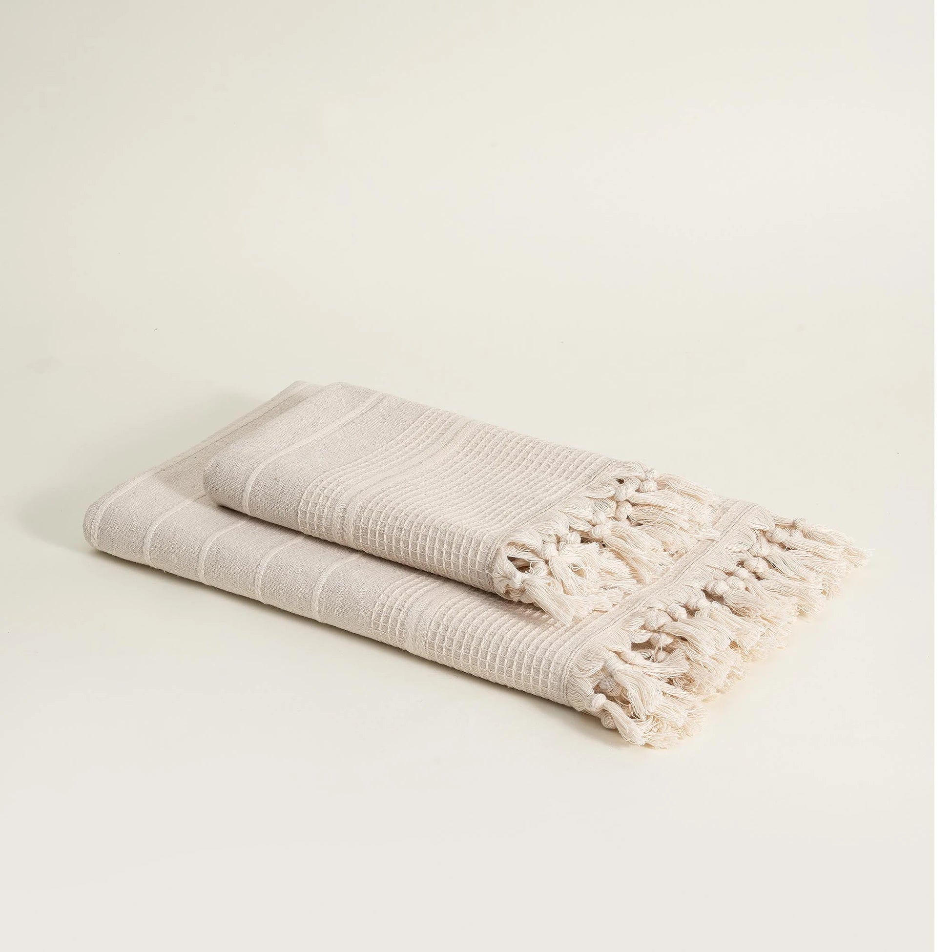Two folded Arden Hemp & Organic Cotton Bath Towels with Tassels in Sand n White, displaying their soft texture and natural colour