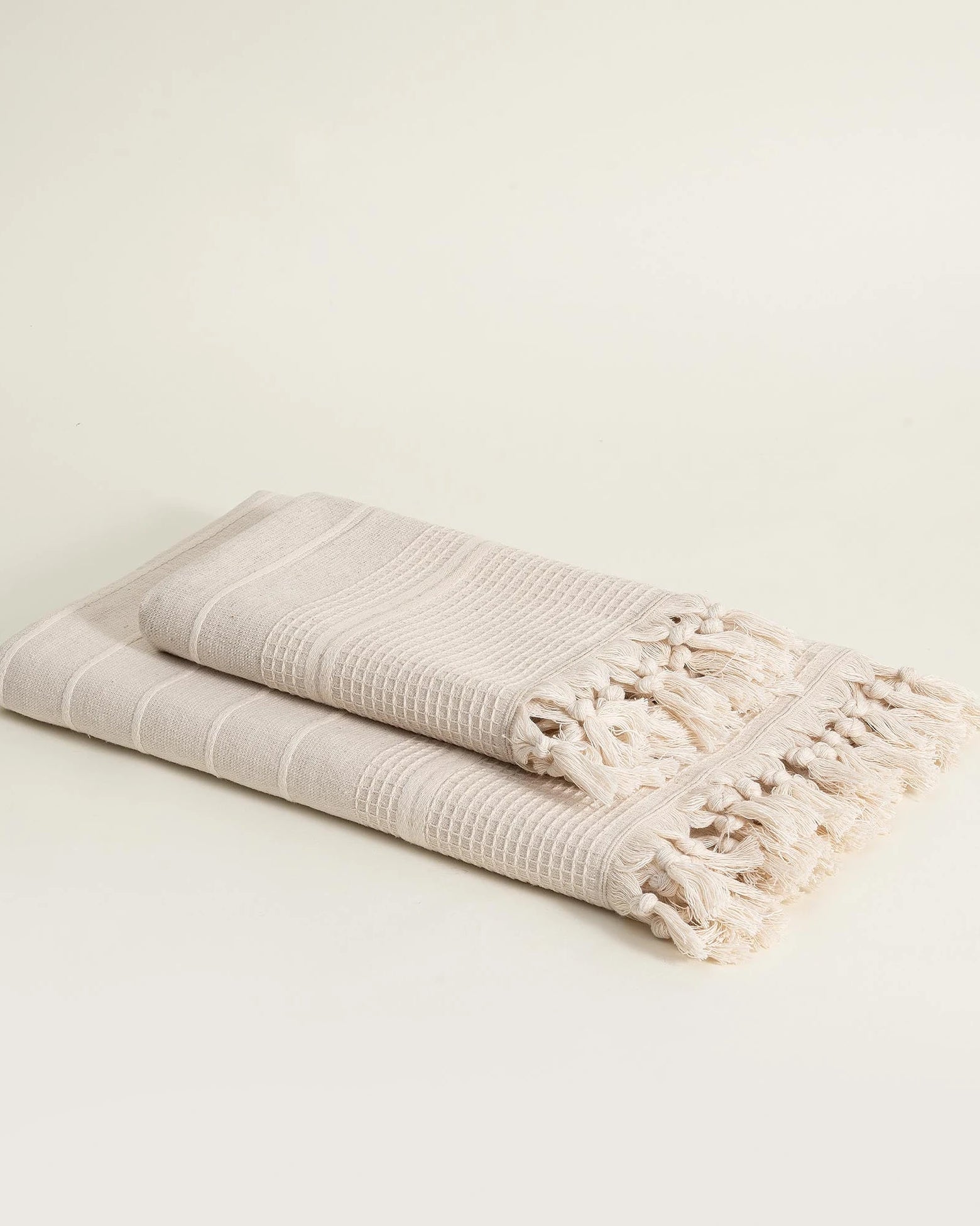 Folded beige towel with tassels on a light beige background
