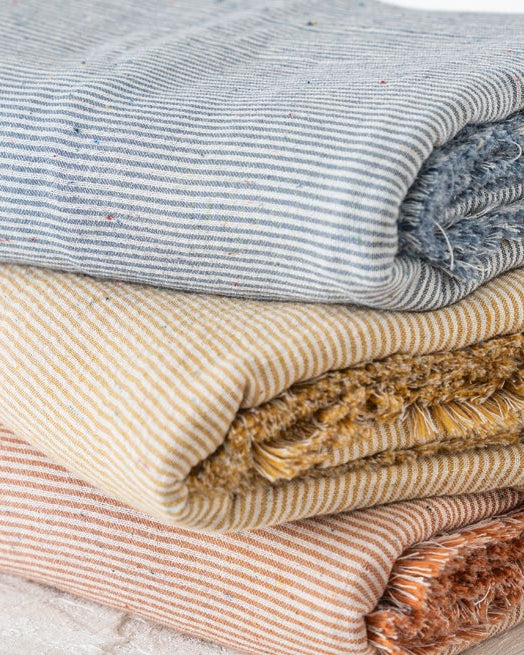 Stack of folded textured blankets in various colors on a light wooden surface