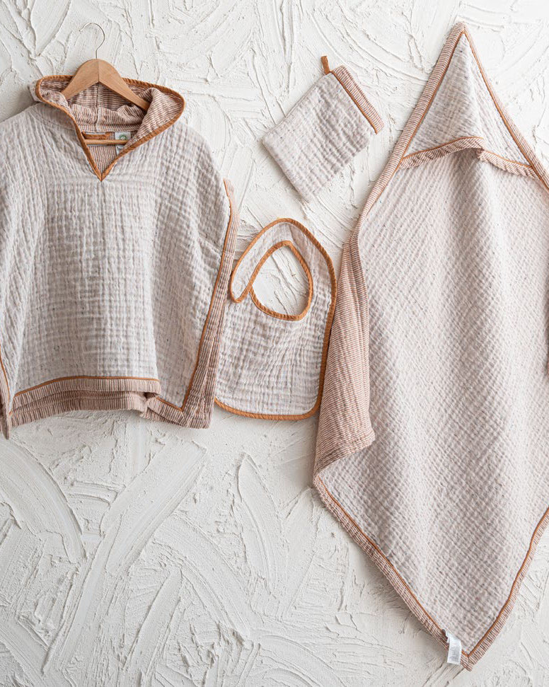Baby clothing set including a poncho, bib, and blanket on a textured white surface.