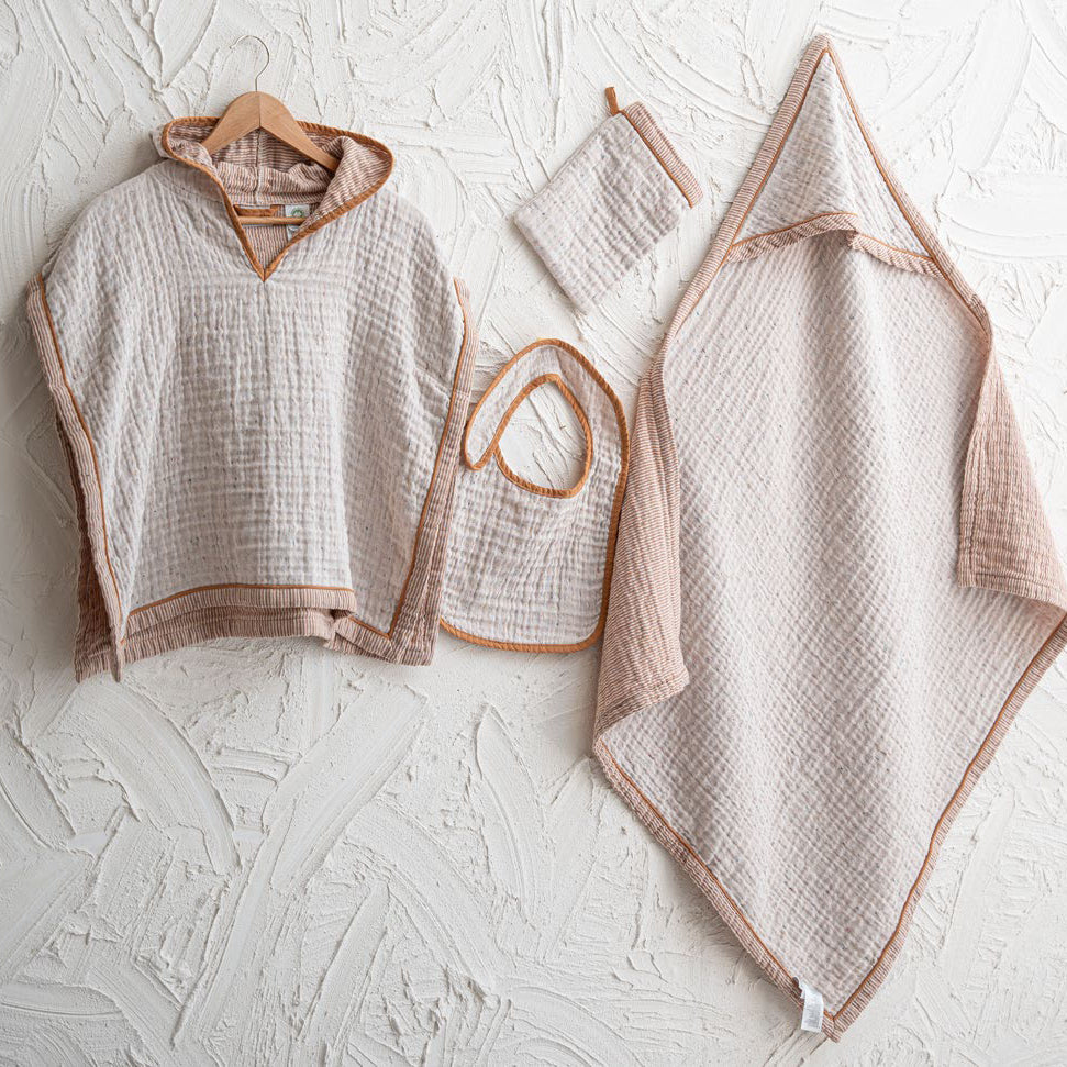 Baby clothing set including a poncho, bib, and blanket on a textured white surface.
