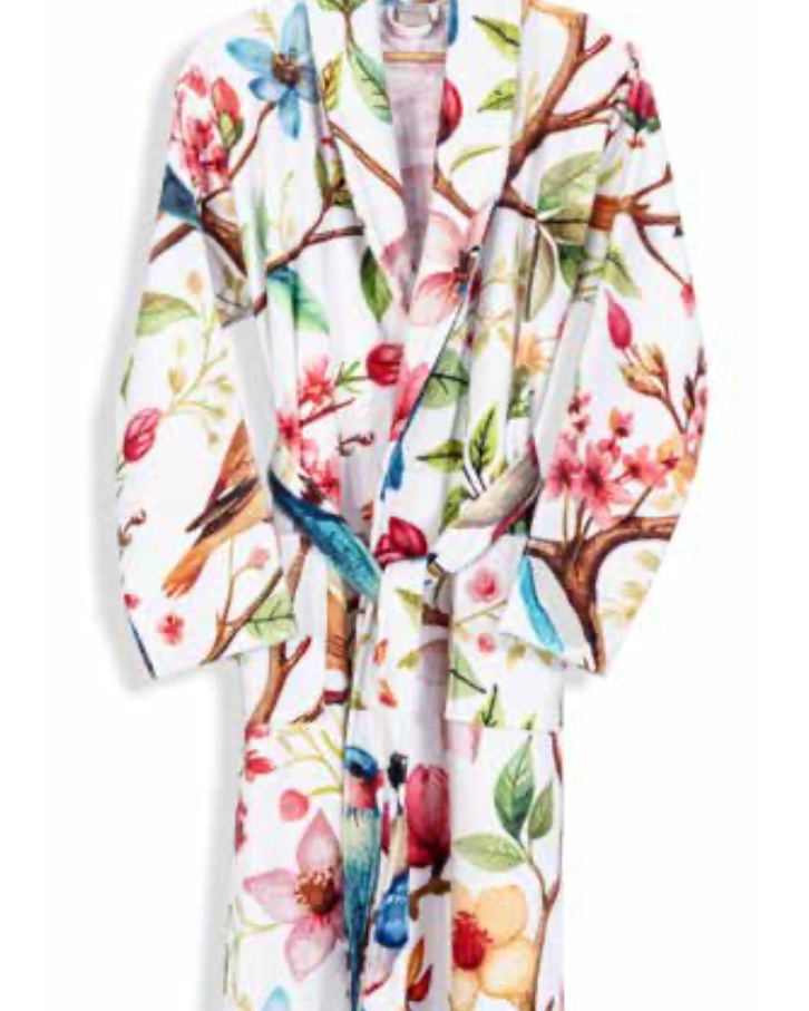 White bathrobe with colorful floral and bird print design hanging on wooden hanger — botanical-inspired sustainable home textile.