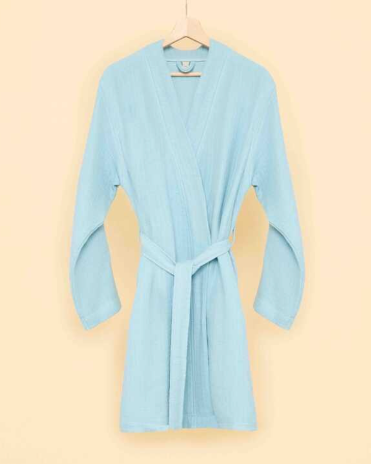 Light blue bathrobe with belt tie on wooden hanger against a soft beige background — minimalist sustainable loungewear aesthetic.