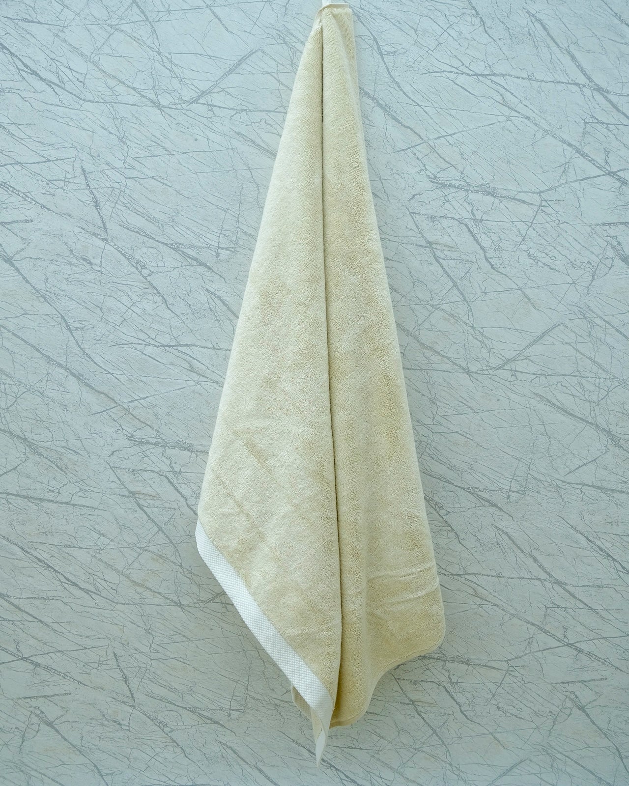 Cream-colored Minoa Home organic cotton hand towel hanging on a textured marble wall, showcasing spa-inspired bathroom decor.