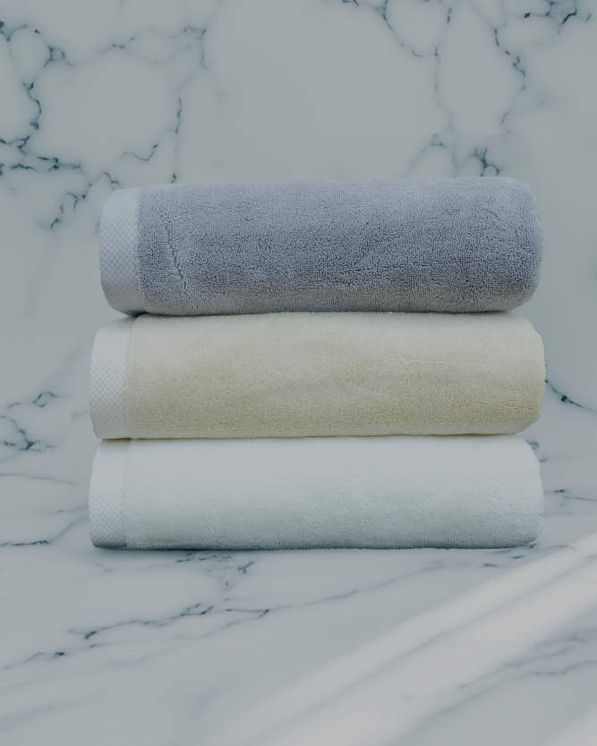 Stack of three luxury organic cotton bath towels in white, cream, and grey from Minoa Home, displayed on a marble background