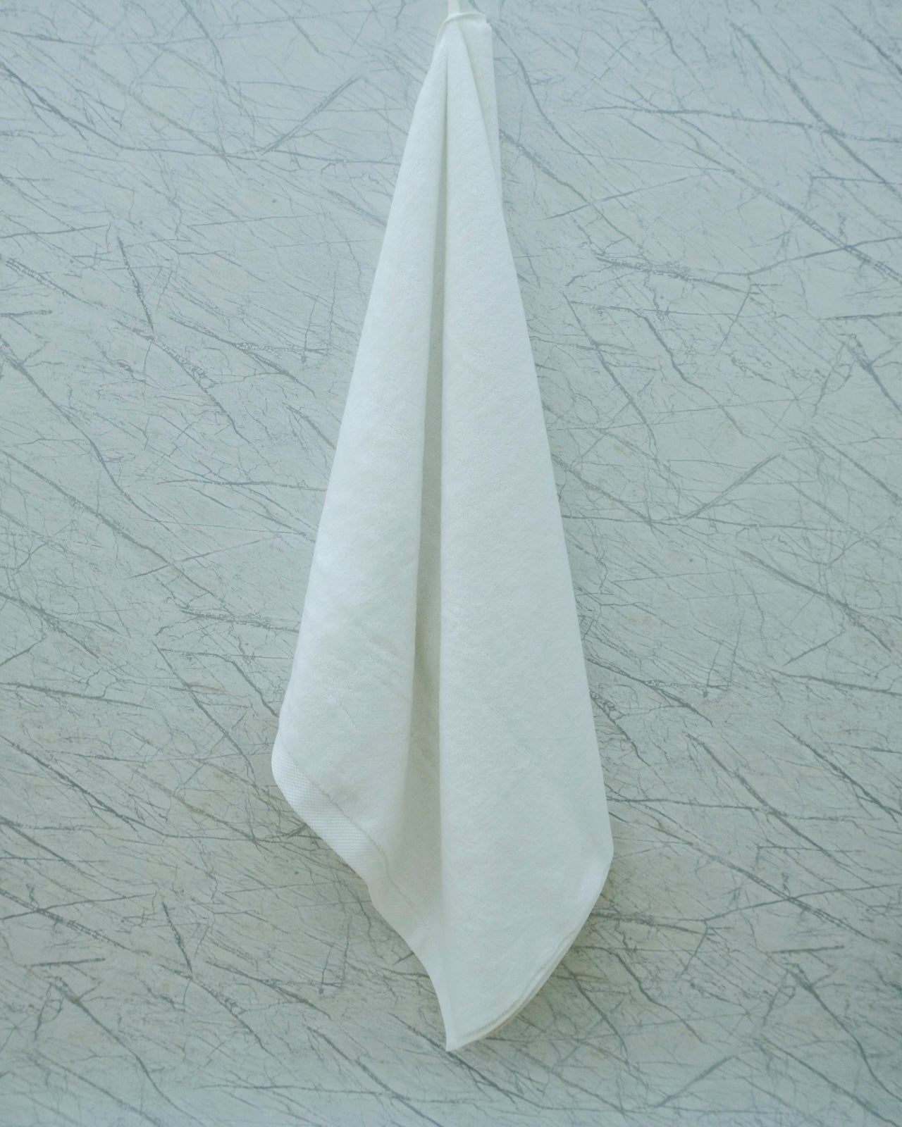 Minimalist display of a white Minoa Home organic cotton hand towel hanging against a textured marble wall.