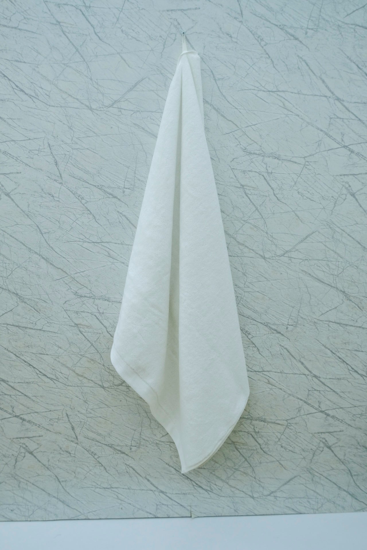 Minimalist display of a white Minoa Home organic cotton hand towel hanging against a textured marble wall.