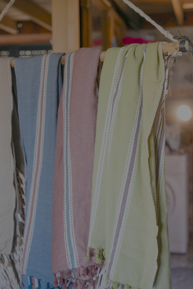 Minoa Home's multicolor peshtemal towels in blue, red, and green hues, handwoven with eco-friendly cotton and detailed white stripes, displayed on a rustic wooden rack.