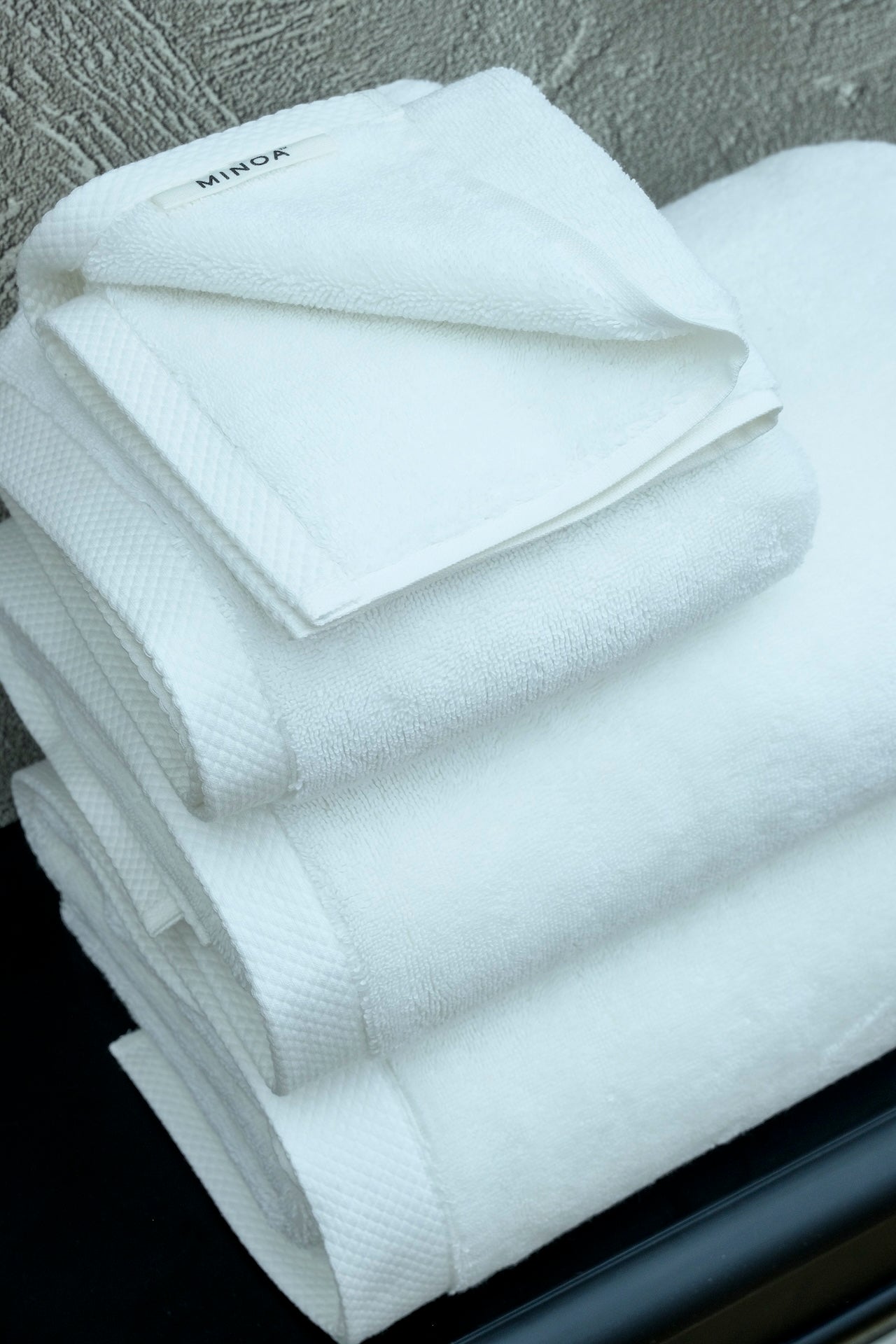 Stack of ultra soft luxury bath towels from Minoa Home made with premium organic cotton, showing the textured detail and Minoa branding tag