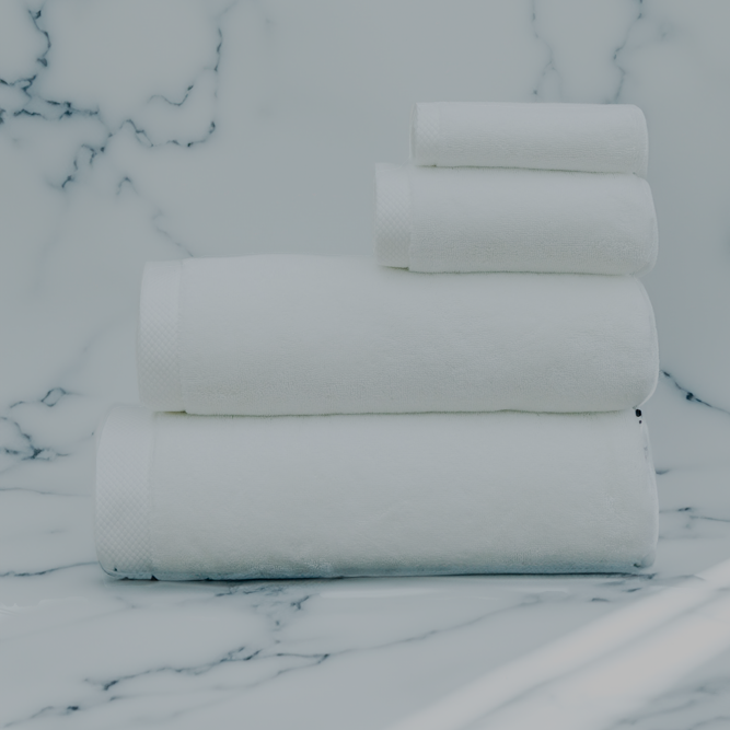Luxurious white organic bath towel set from Minoa Home, made with premium cotton, neatly stacked on a marble surface, including bath, hand, and face towels