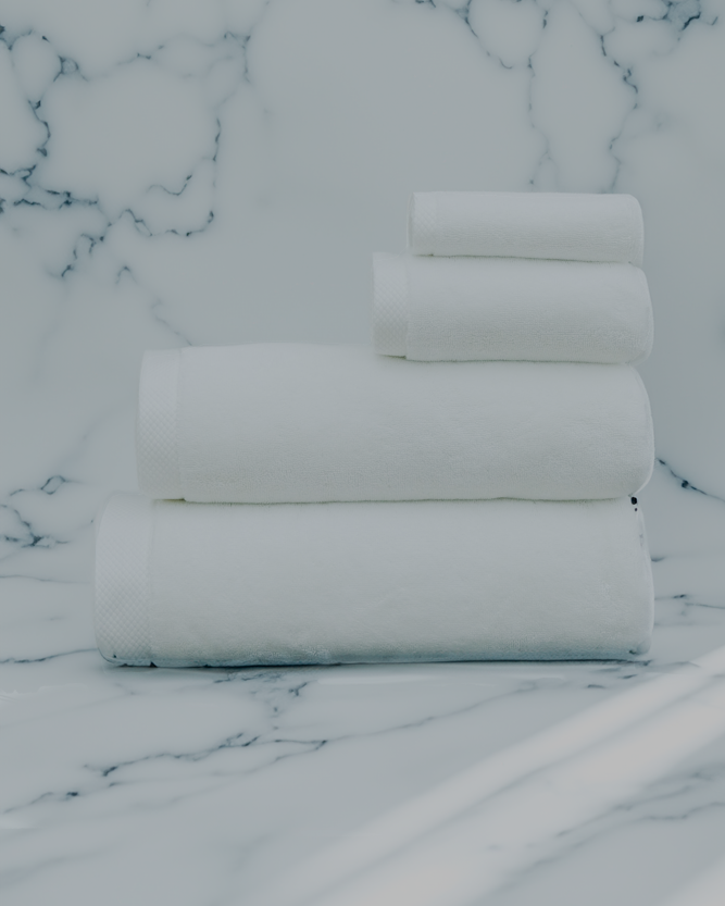 Luxurious white organic bath towel set from Minoa Home, made with premium cotton, neatly stacked on a marble surface, including bath, hand, and face towels