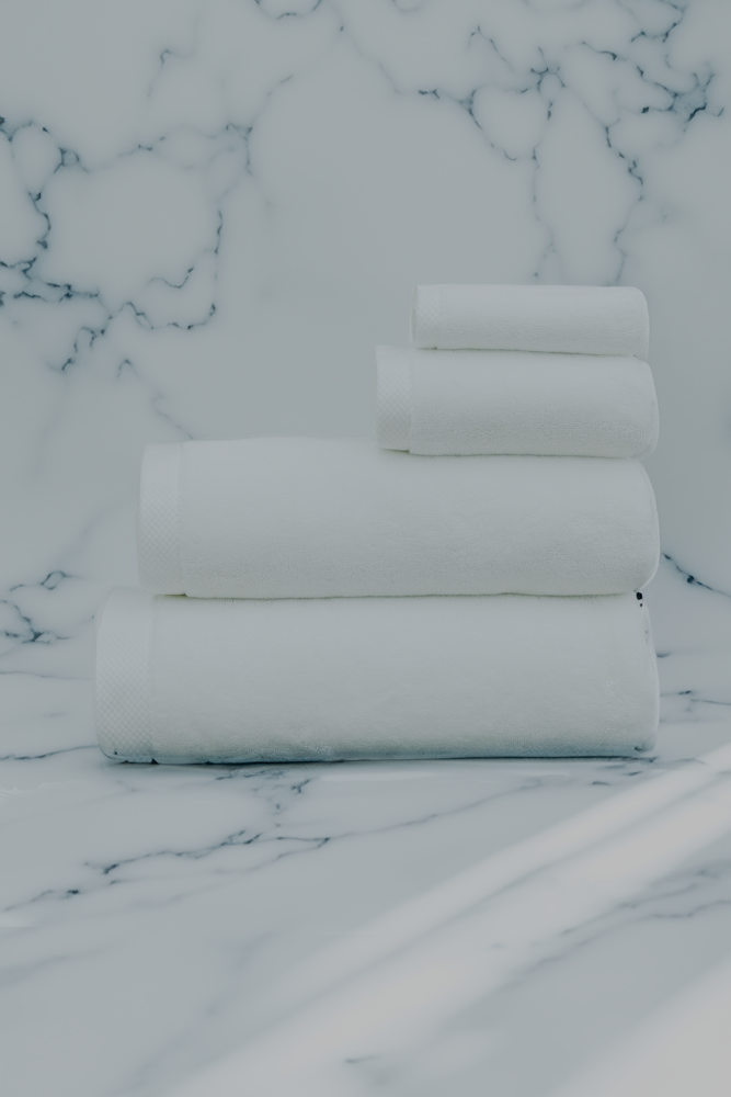 Luxurious white organic bath towel set from Minoa Home, made with premium cotton, neatly stacked on a marble surface, including bath, hand, and face towels