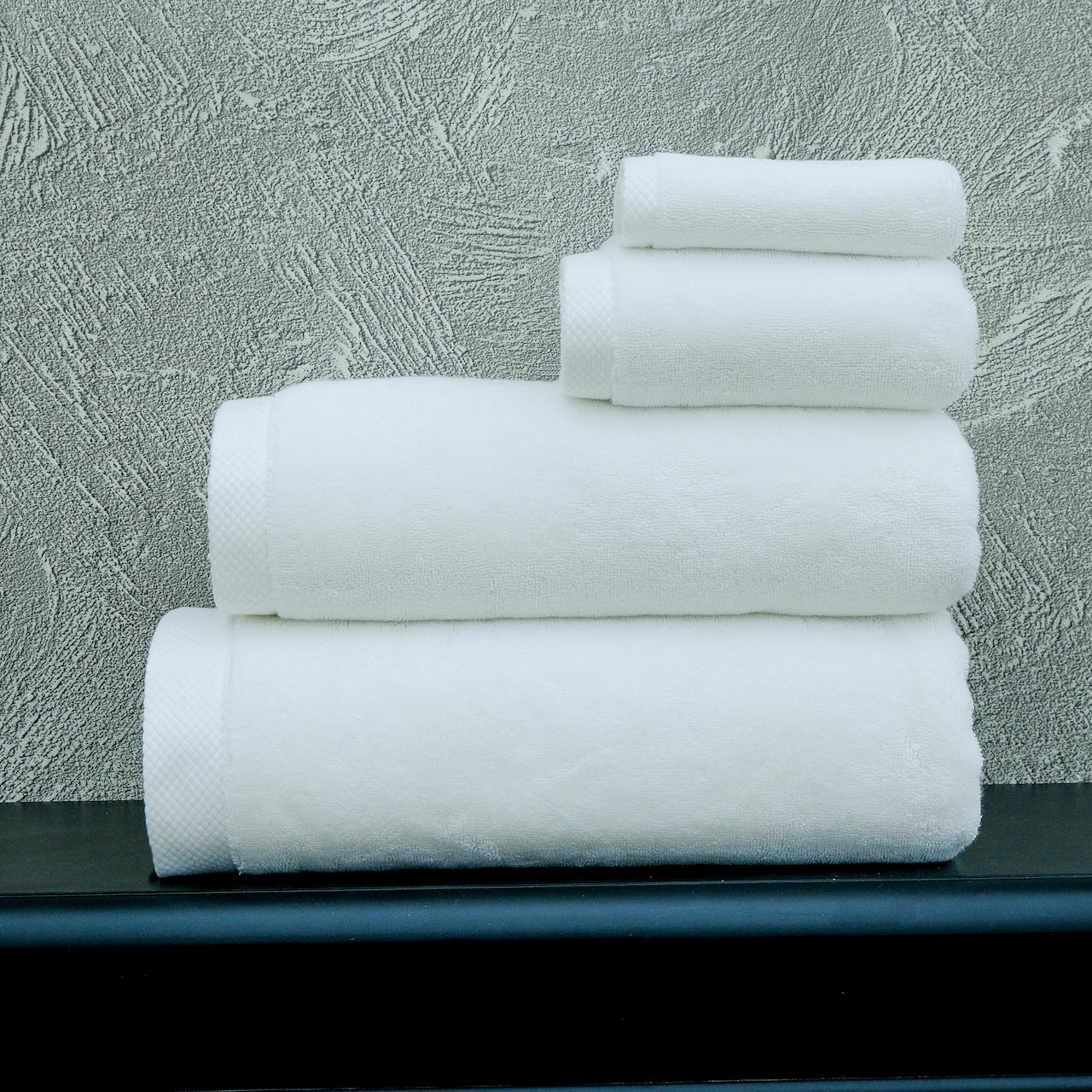 Stack of white towels on a black surface with a textured gray wall background