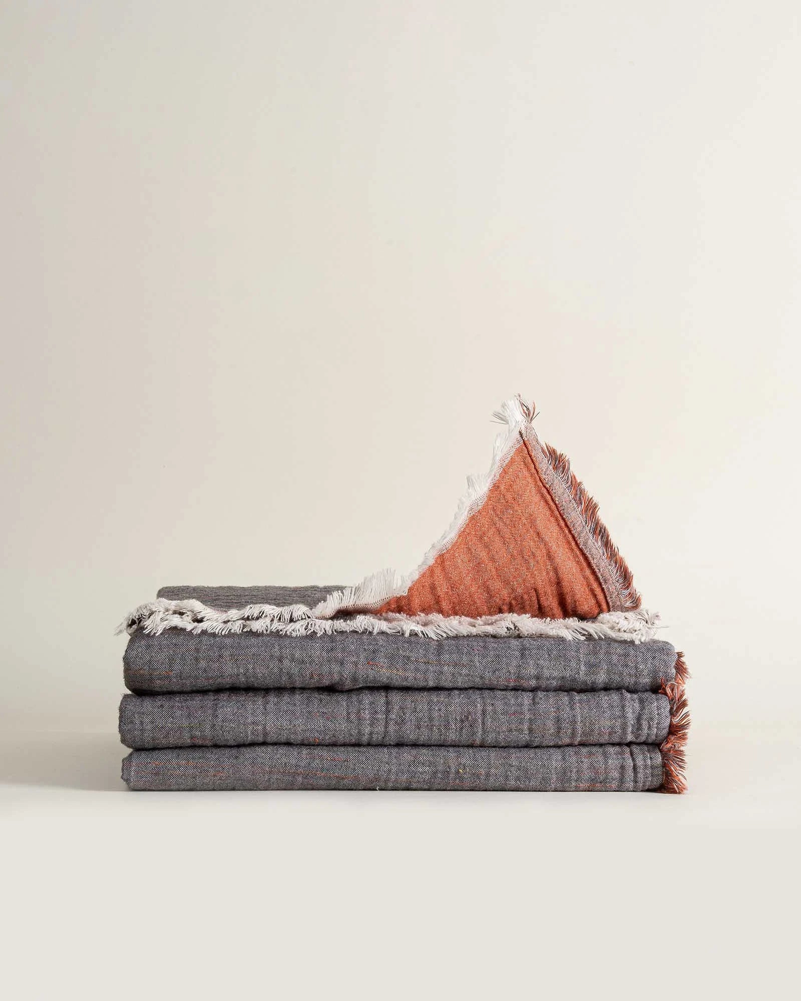 Folded reversible Muna organic gauze bed spread in Terra, soft texture, earthy hue, versatile design with organic cotton sheets.