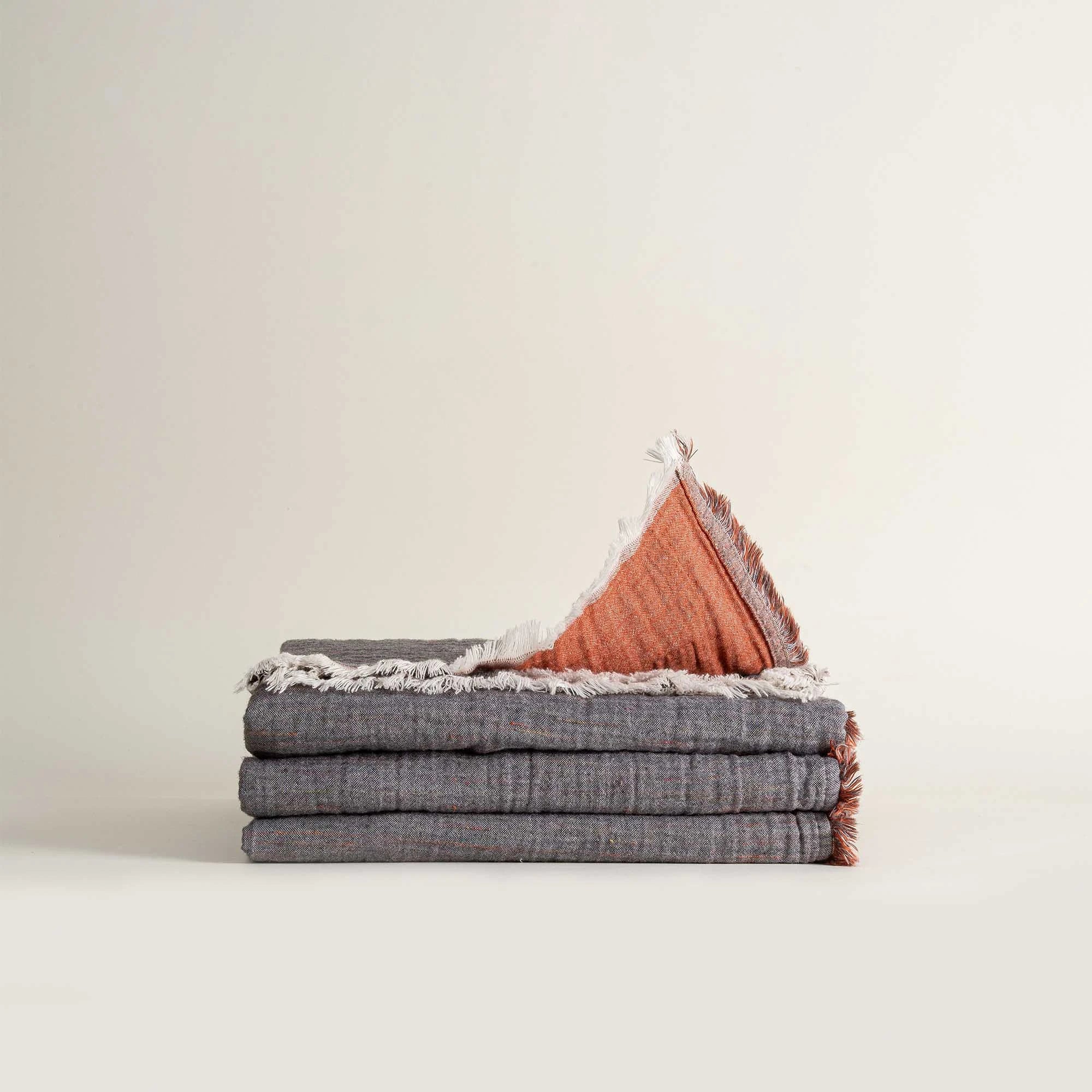 Folded reversible Muna organic gauze bed spread in Terra, soft texture, earthy hue, versatile design with organic cotton sheets.