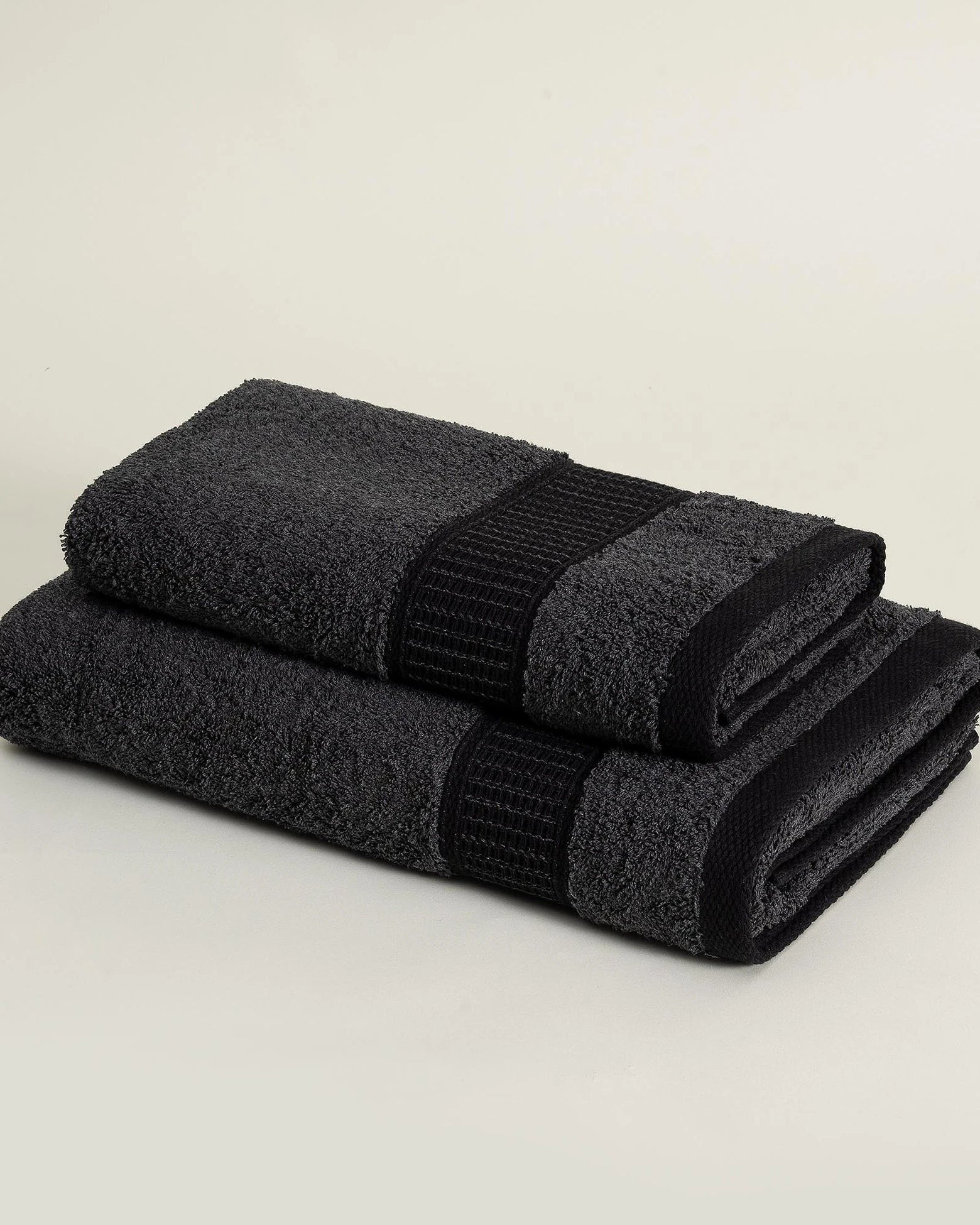 Two folded Minoa sustainable luxury bath towels from the Naia and cotton collection in Dark Pearl, highlighting soft texture, elegant color, and premium quality fabric