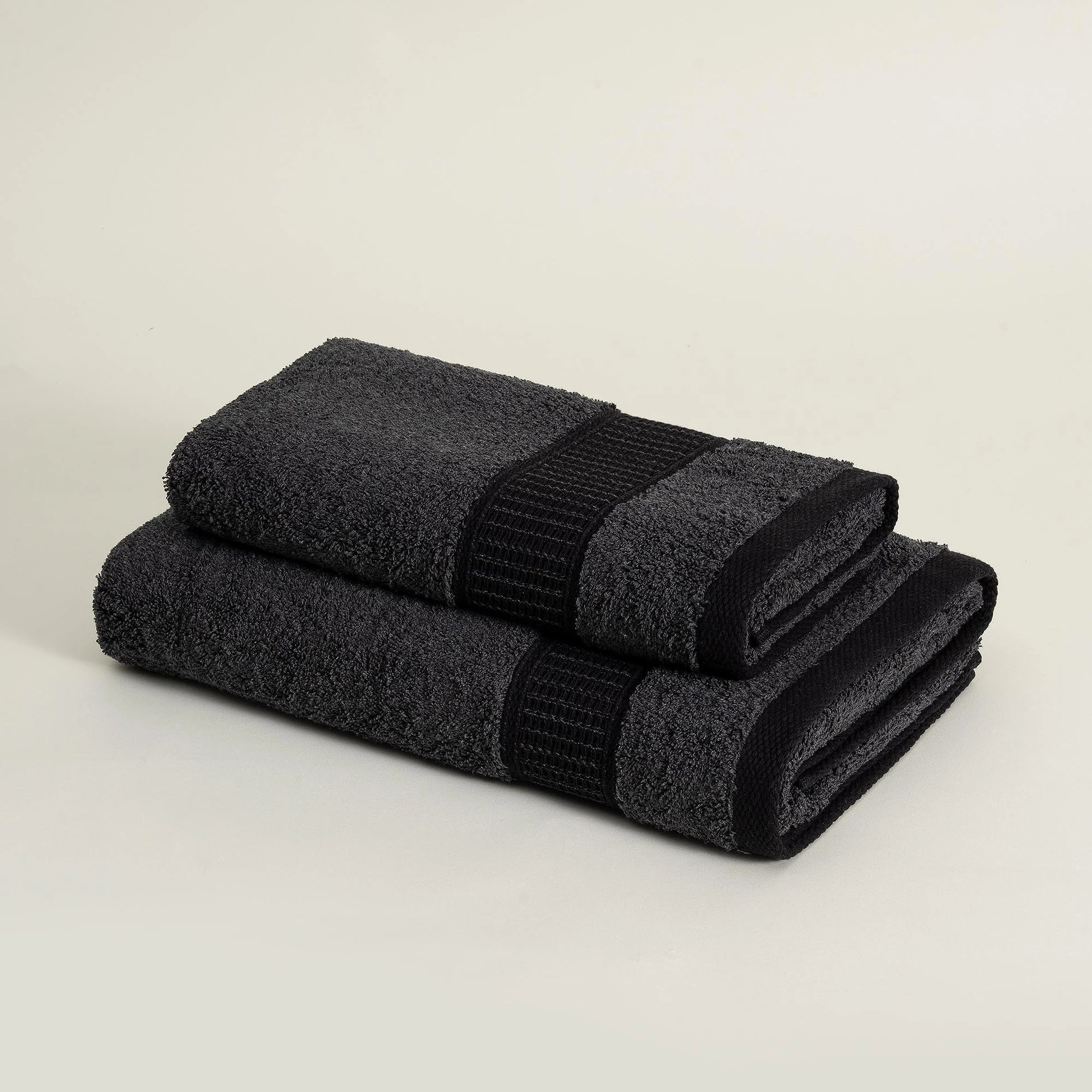 Two folded Minoa sustainable luxury bath towels from the Naia and cotton collection in Dark Pearl, highlighting soft texture, elegant color, and premium quality fabric