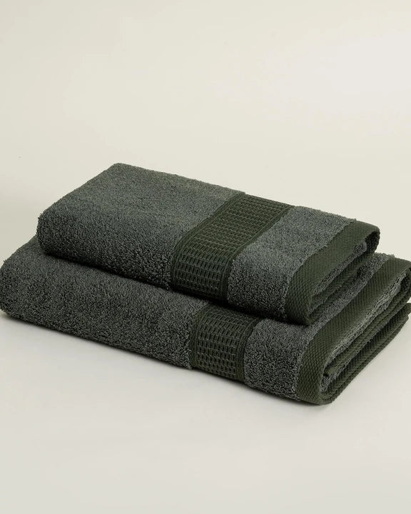 Two folded dark green towels on a light beige background