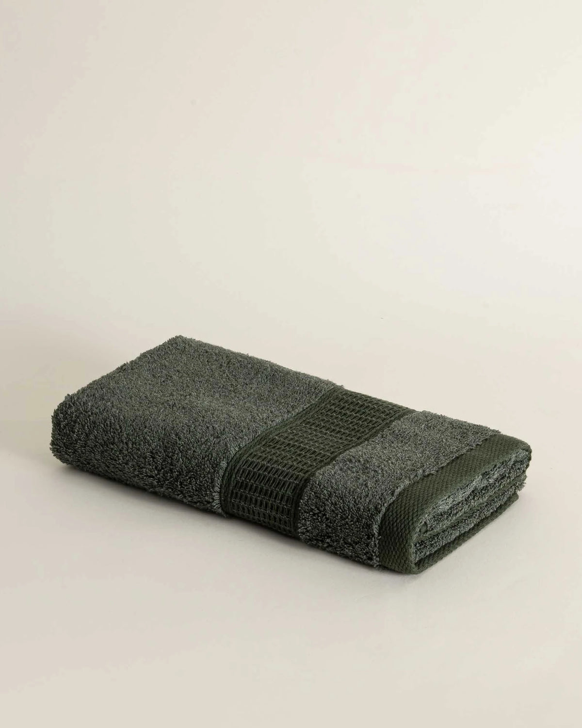 Folded dark green towel on a light beige background