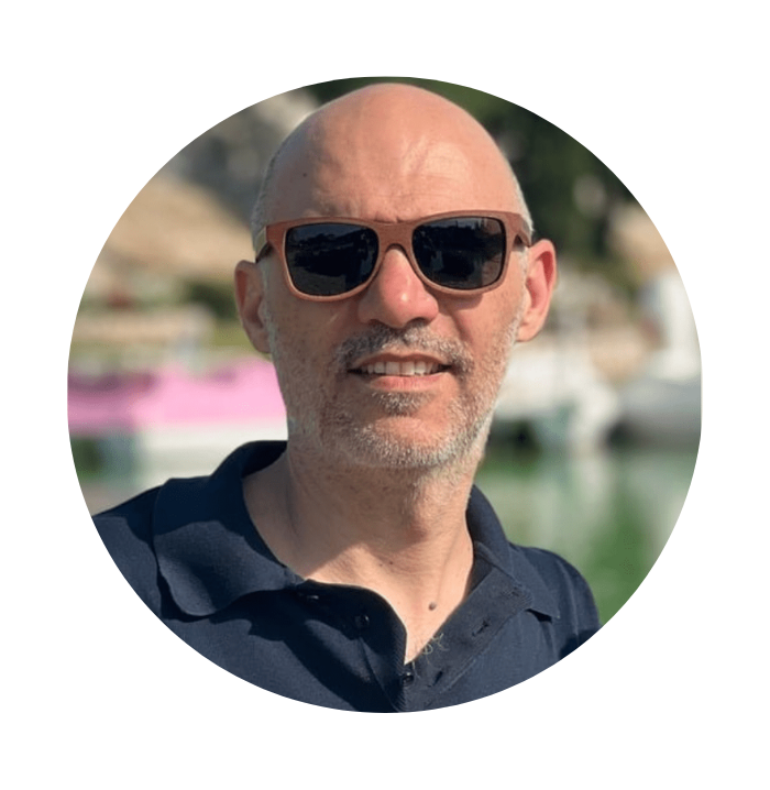 Man wearing sunglasses and a dark polo shirt with a blurred outdoor background