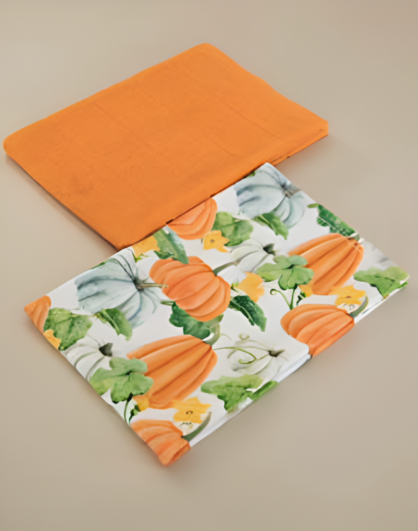 Two kitchen towels, one orange and one with pumpkin pattern, on a beige surface.