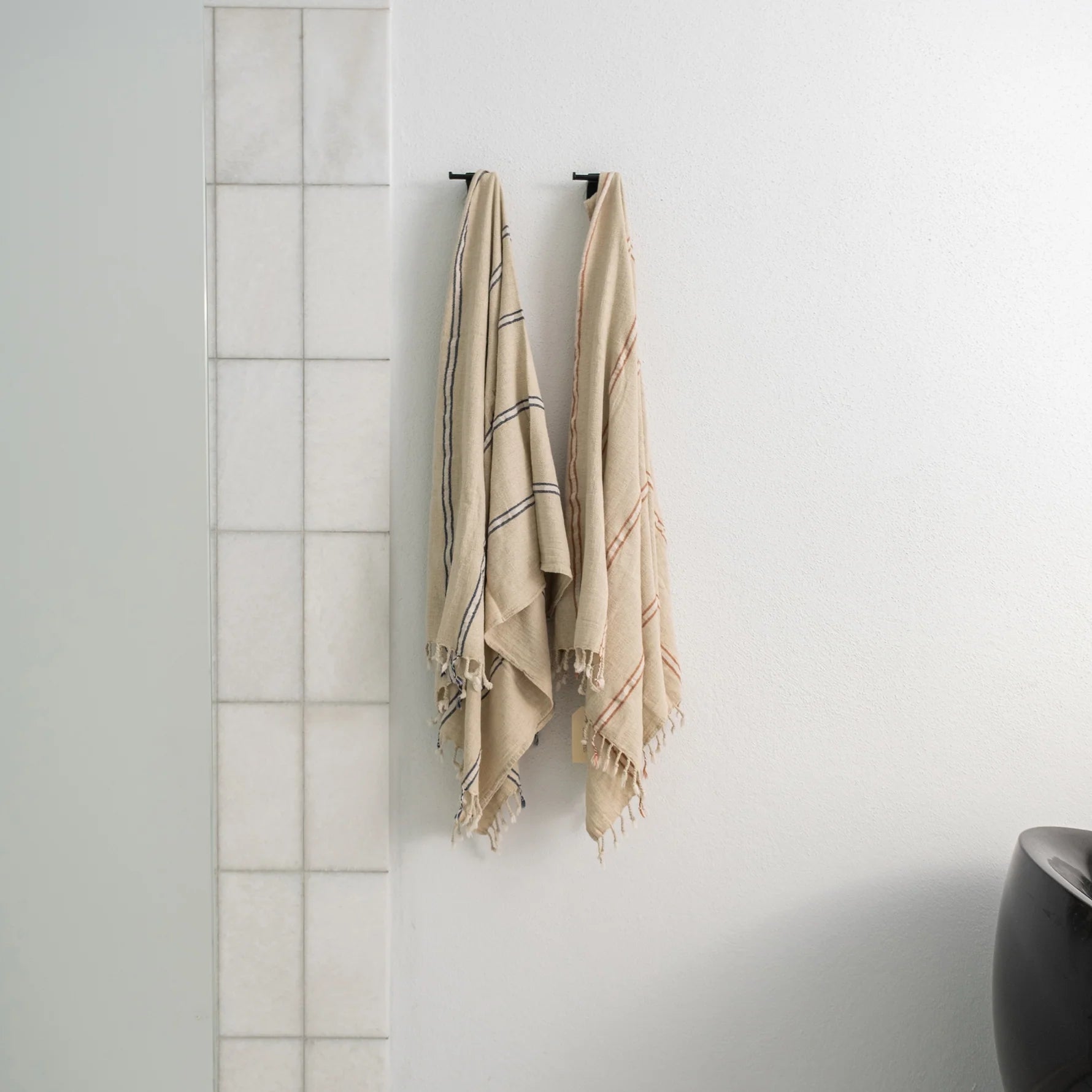 Two sustainable luxury Anakao 215 gram Aegean Cotton and Linen Turkish luxury bath towels hanging on a bathroom wall showcasing their soft texture and premium quality